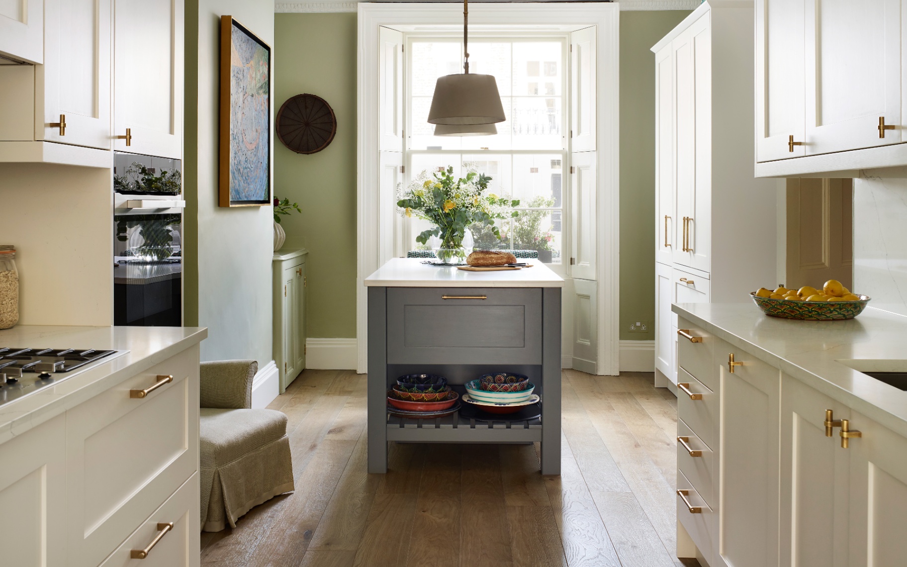 a small kitchen with white cabinets, wooden floor, a grey kitchen island and a pendant light above it