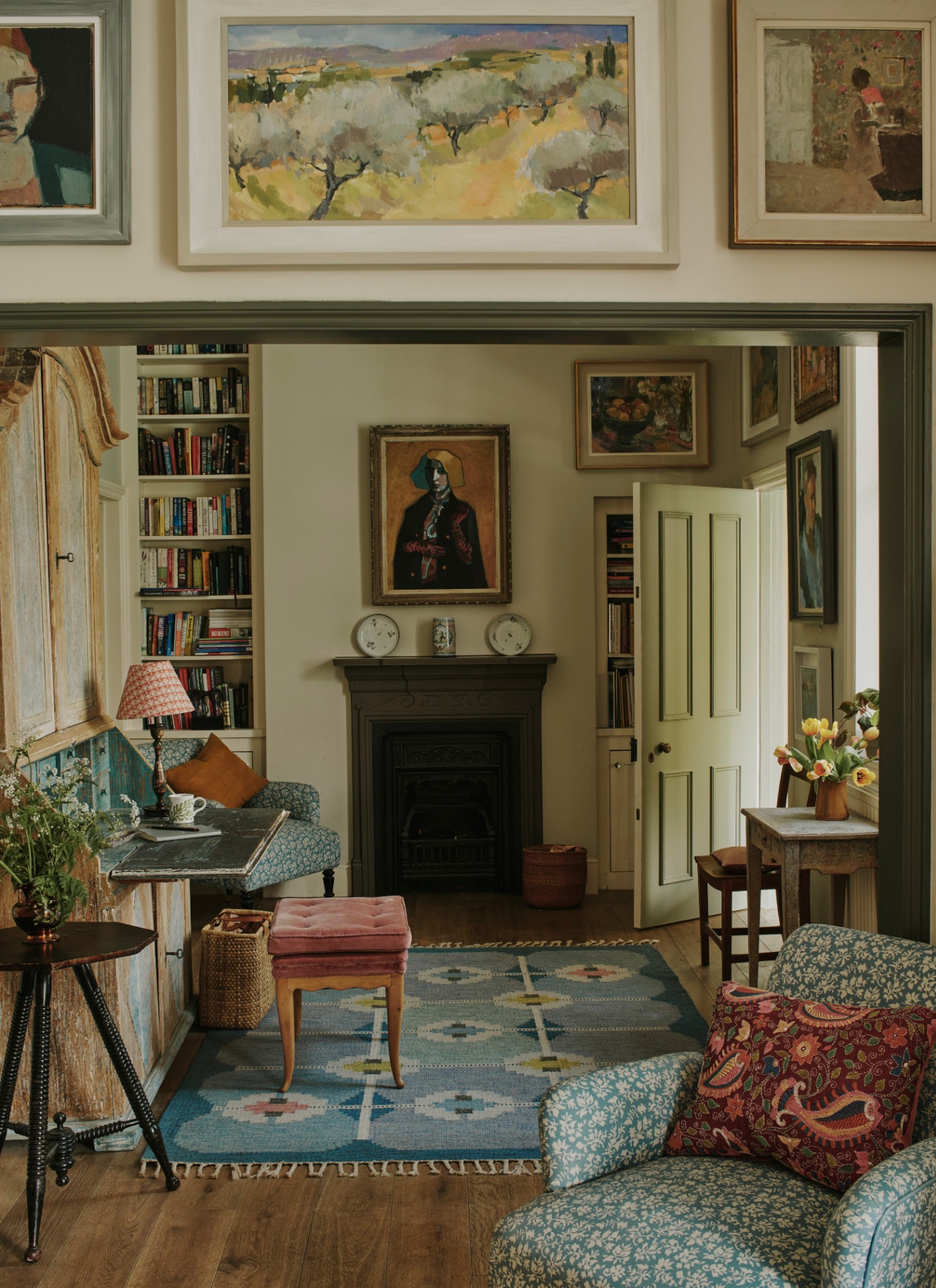 a study with lots of paitnings on the walls, a shabby office bureau and a large fireplace