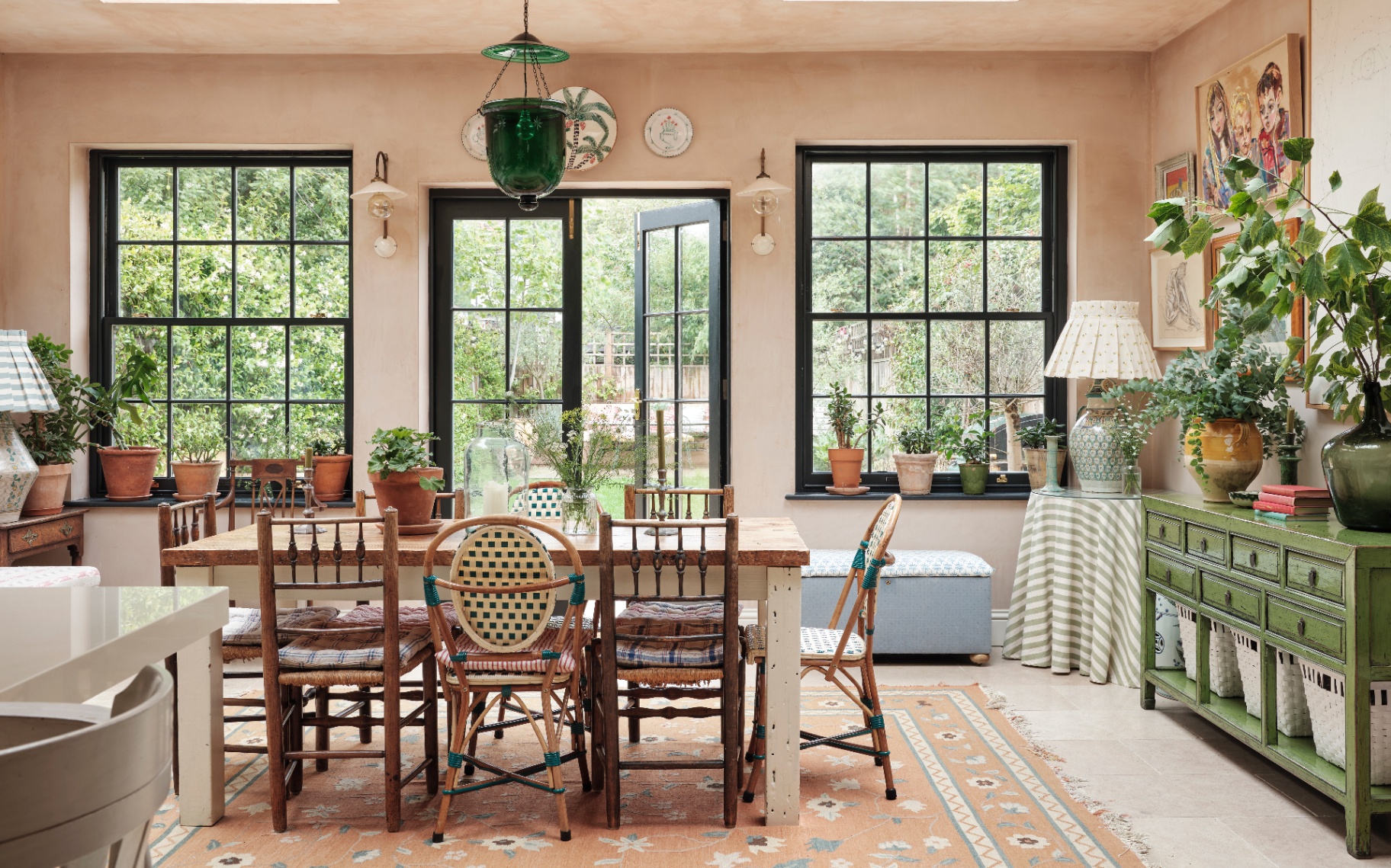a dining room with large frenh doors looking out to a garden, a long dining table with rattan chairs and a large green glass pendant