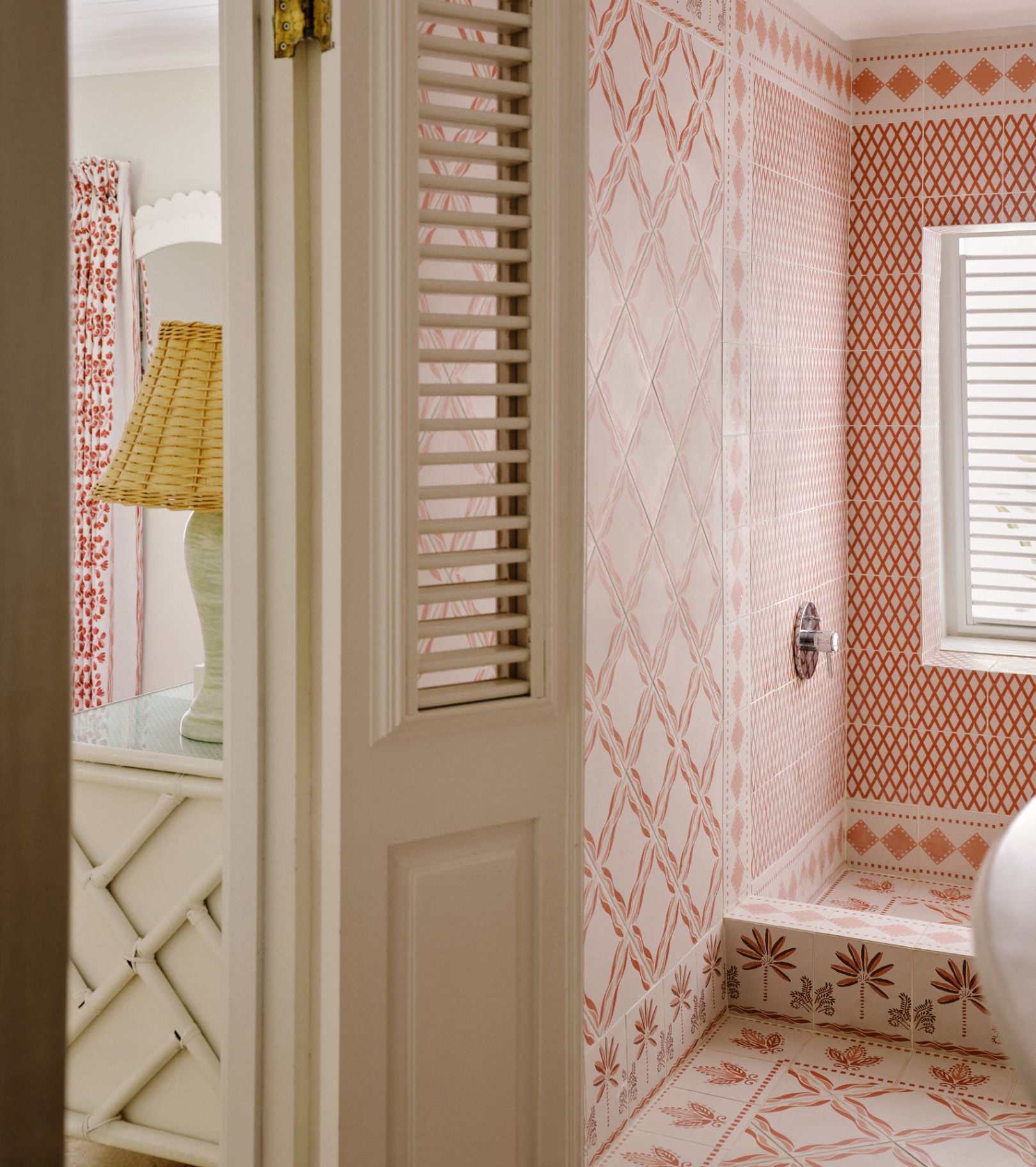 a en suite with red and white and pink patterned all over tiles looking out into a pink and white bedroom