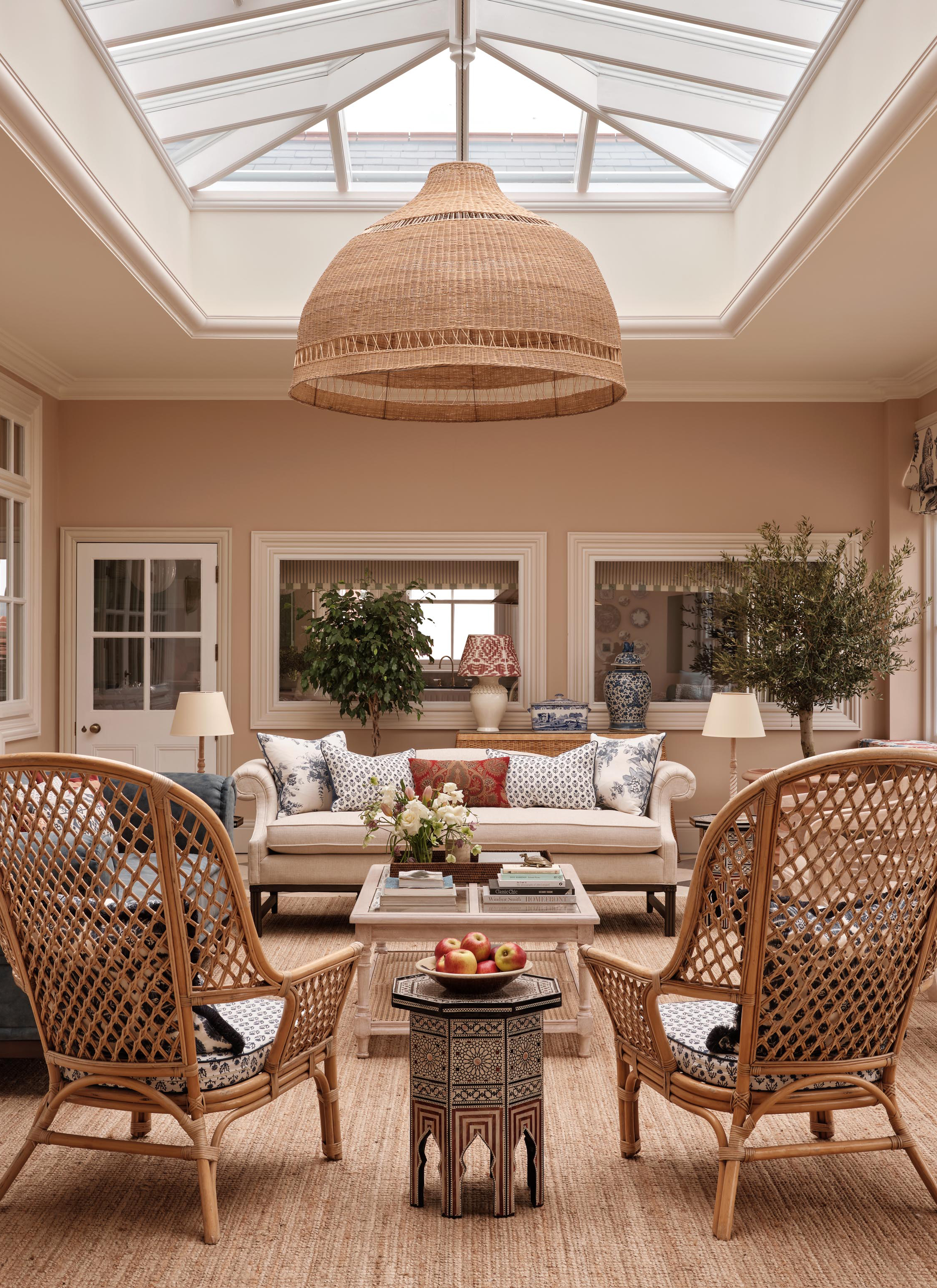 a living room with beige walls and a large skylight with a large rattan pendant hanging from the ceiling and two cane armchairs