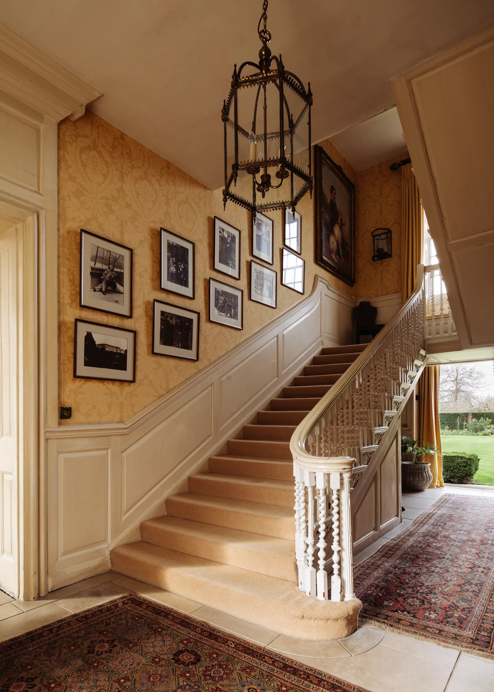 the grand hallway of Ormeley Lodge, Richmond, with a sweeping white staircase, yellow wallpaper and a large pendant