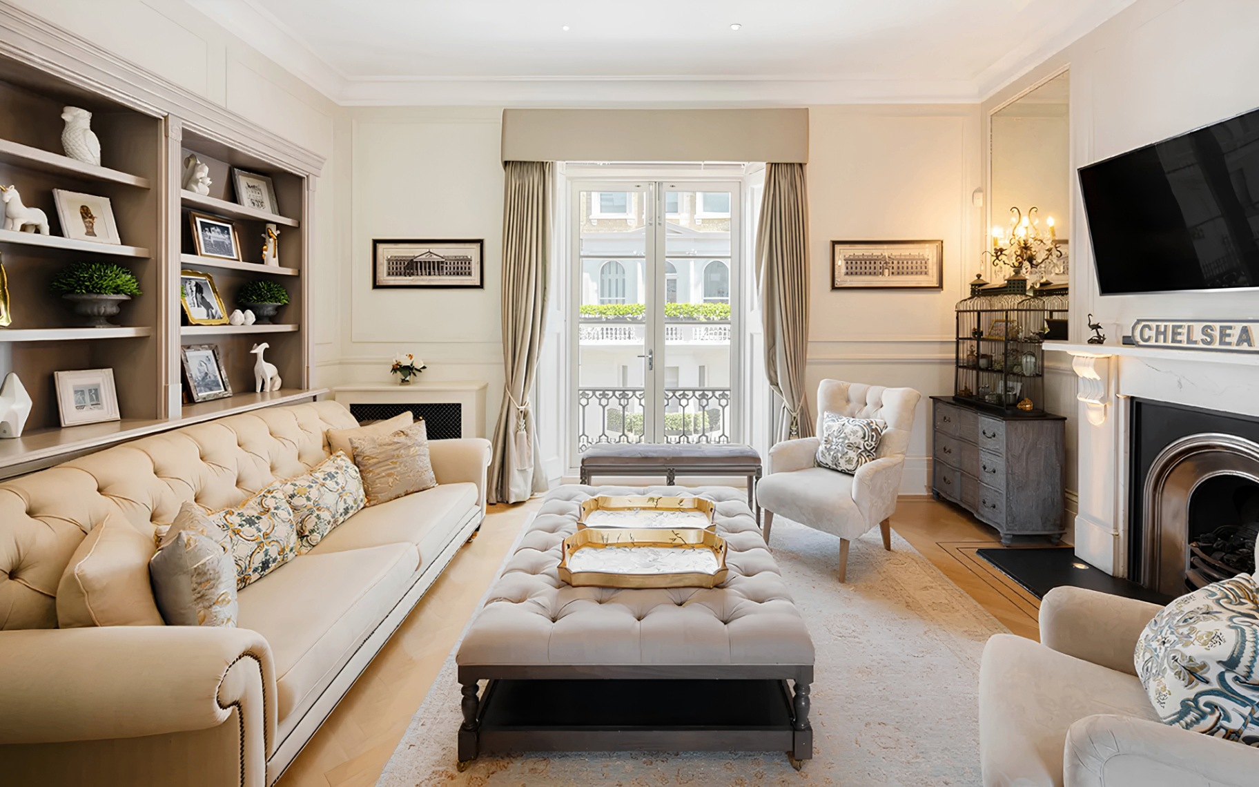 a drawing room in a knightsbridge townhouse with along cream sofa, a shelving unit across the back wall and an upholstered coffee table