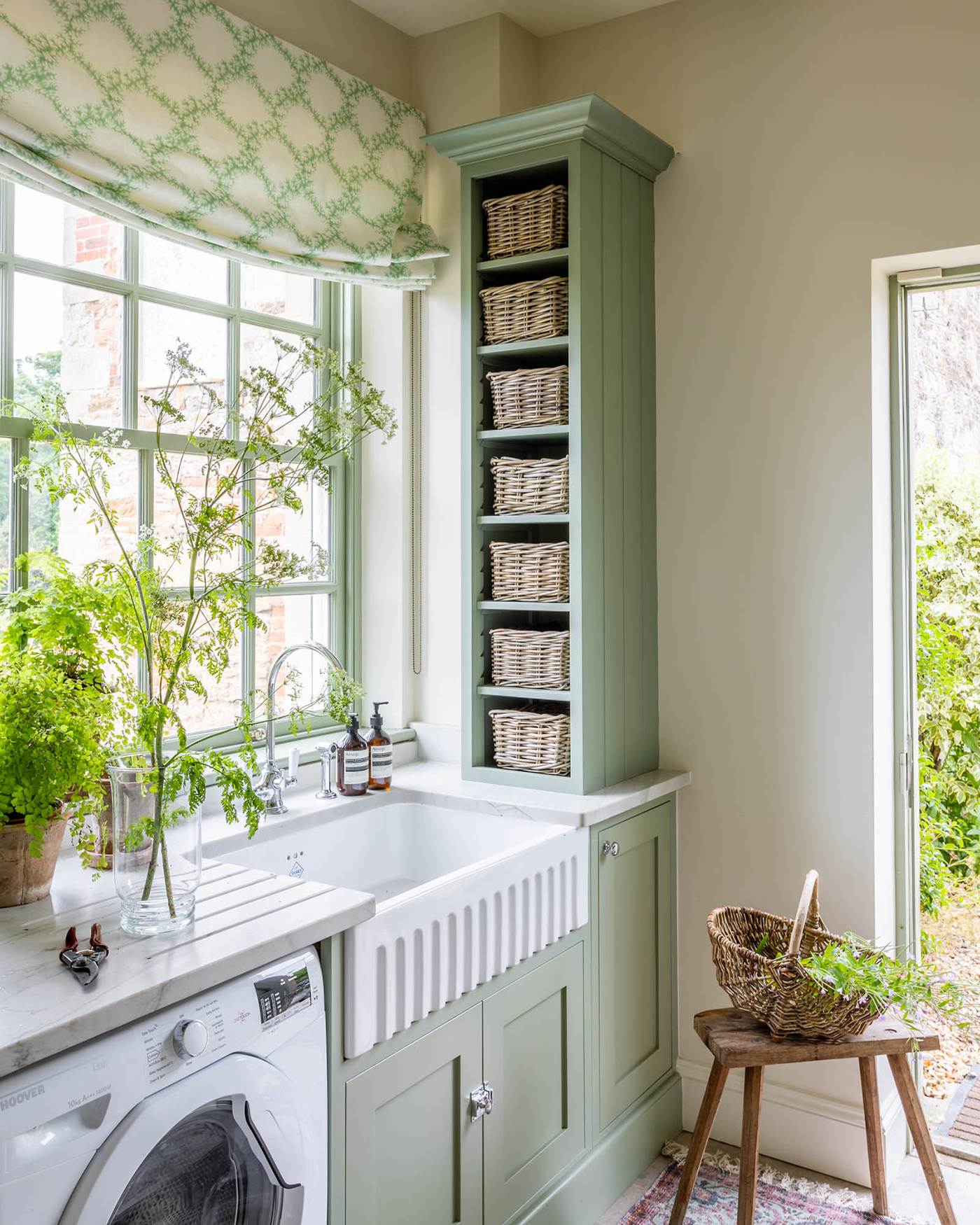 a sage green utility room with a county top built in unit with wicker baskets