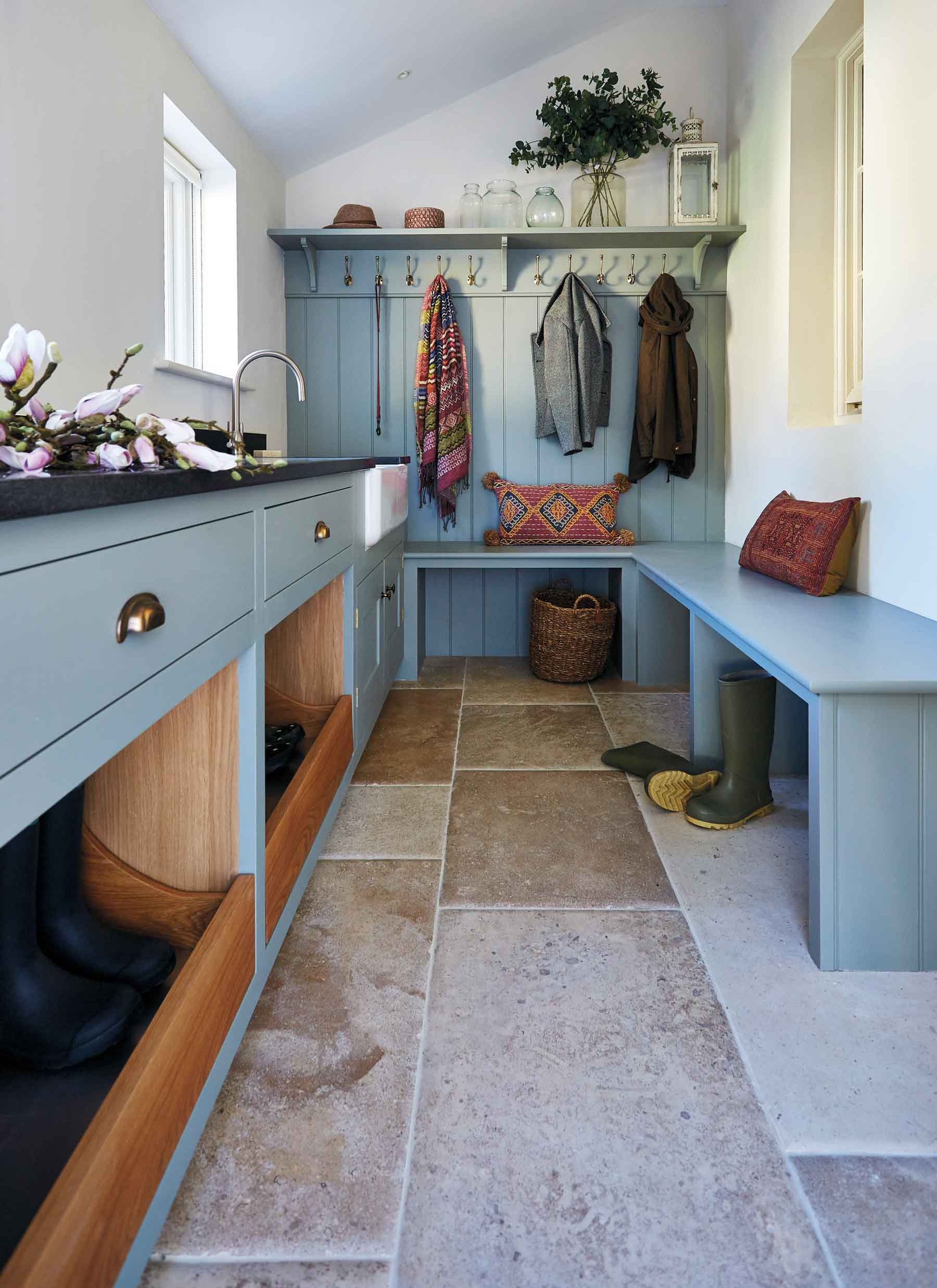 a bootroom with pale stone flooring, pale blue cabinetry and coats hanging from hooks