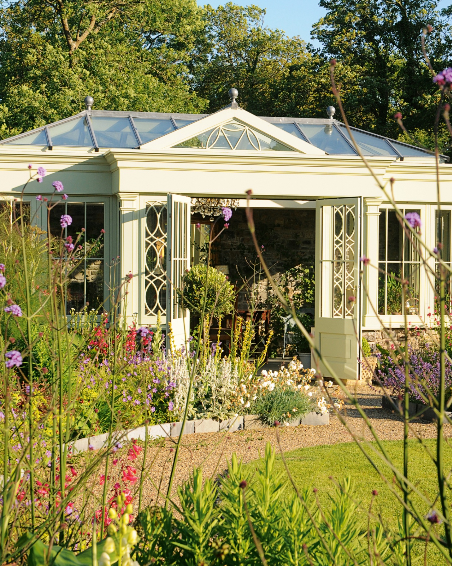 a garden room seen from the garden, with the doors open surrounding by summer flowers
