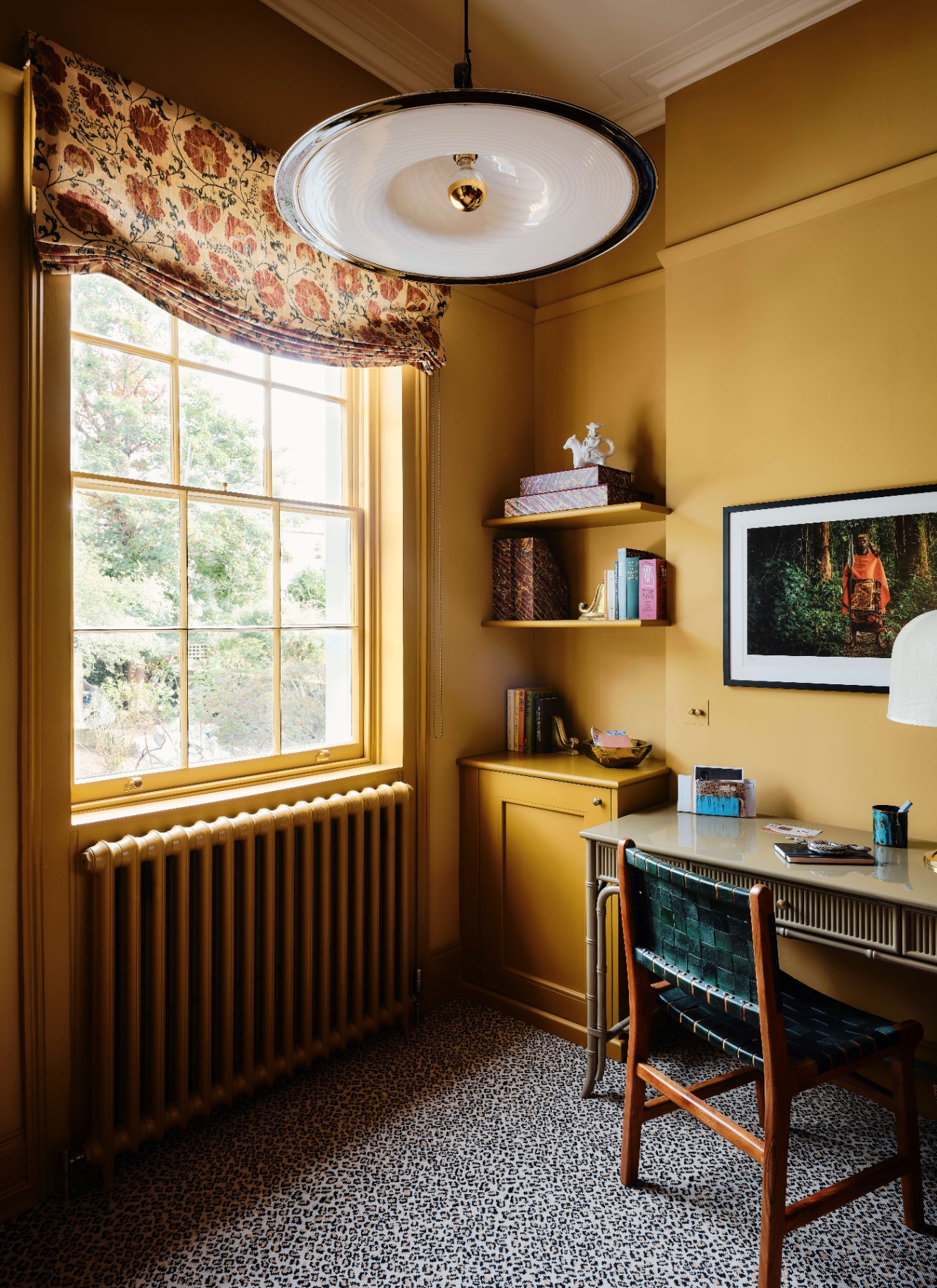 a home office with ochre yellow colour drenched walls, windows, shelves and radiator and a black and white animal print carpet