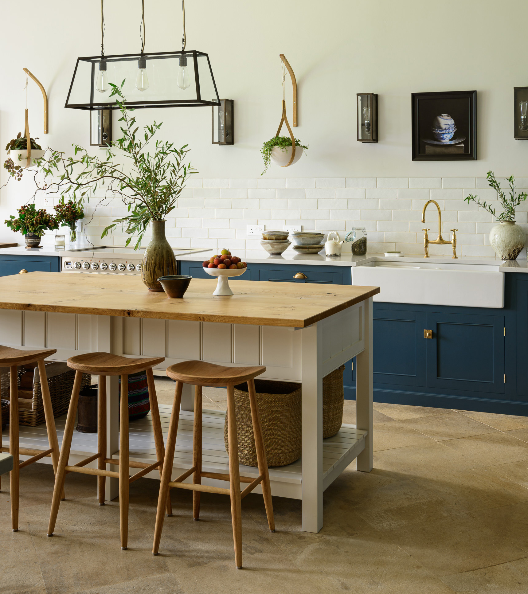 a white kitchen with dark blue cabinetry, a white and brown butchers block with wooden stools next to it and a large kitchen pendant light