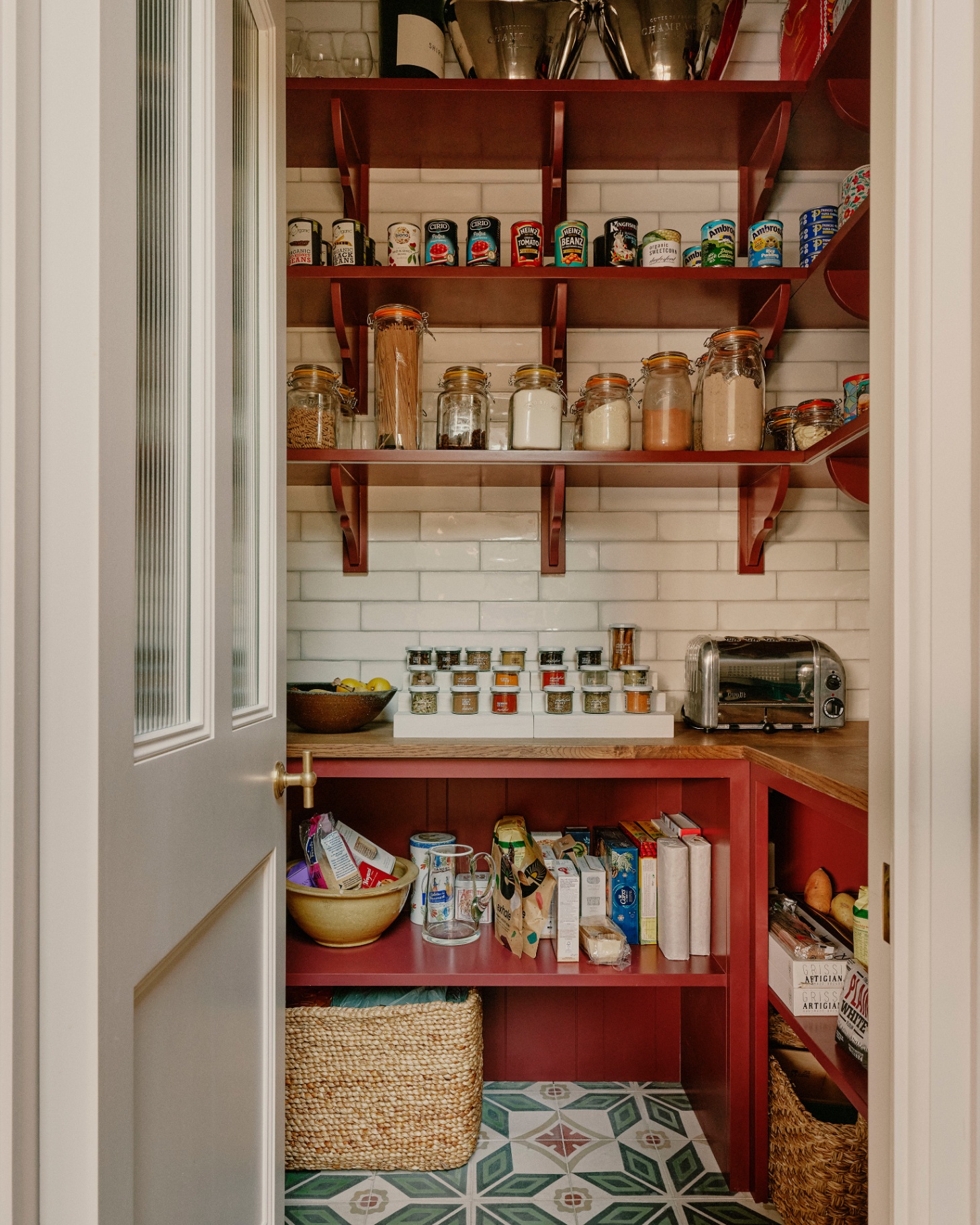 a pantry with red painted shelves filled with food and jars, white tiles and green patterned tiled floor