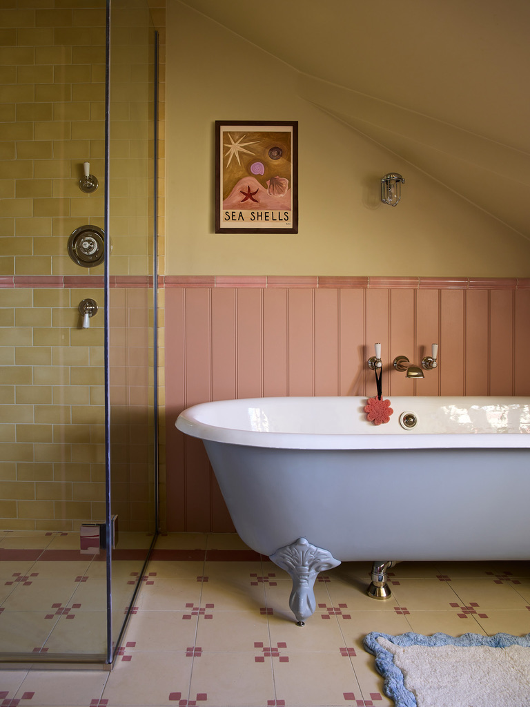 a painted roll top bathtub is the focal point of this bathroom, patterned tiles are pictured and a large shower, pictures can be seen on the walls