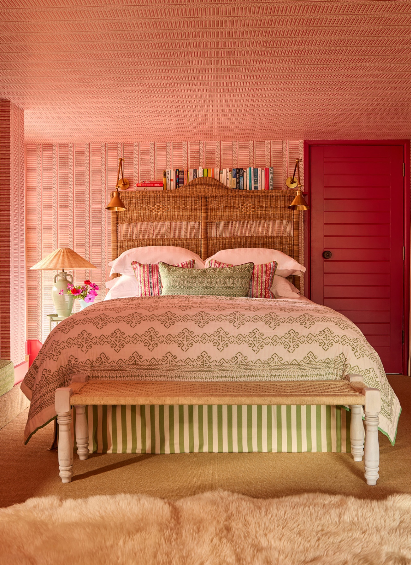 A BEDROOM with pink and white micro stripe wallpaper on the walls and ceiling and a bed with a large rattan headboard and white and green bedding
