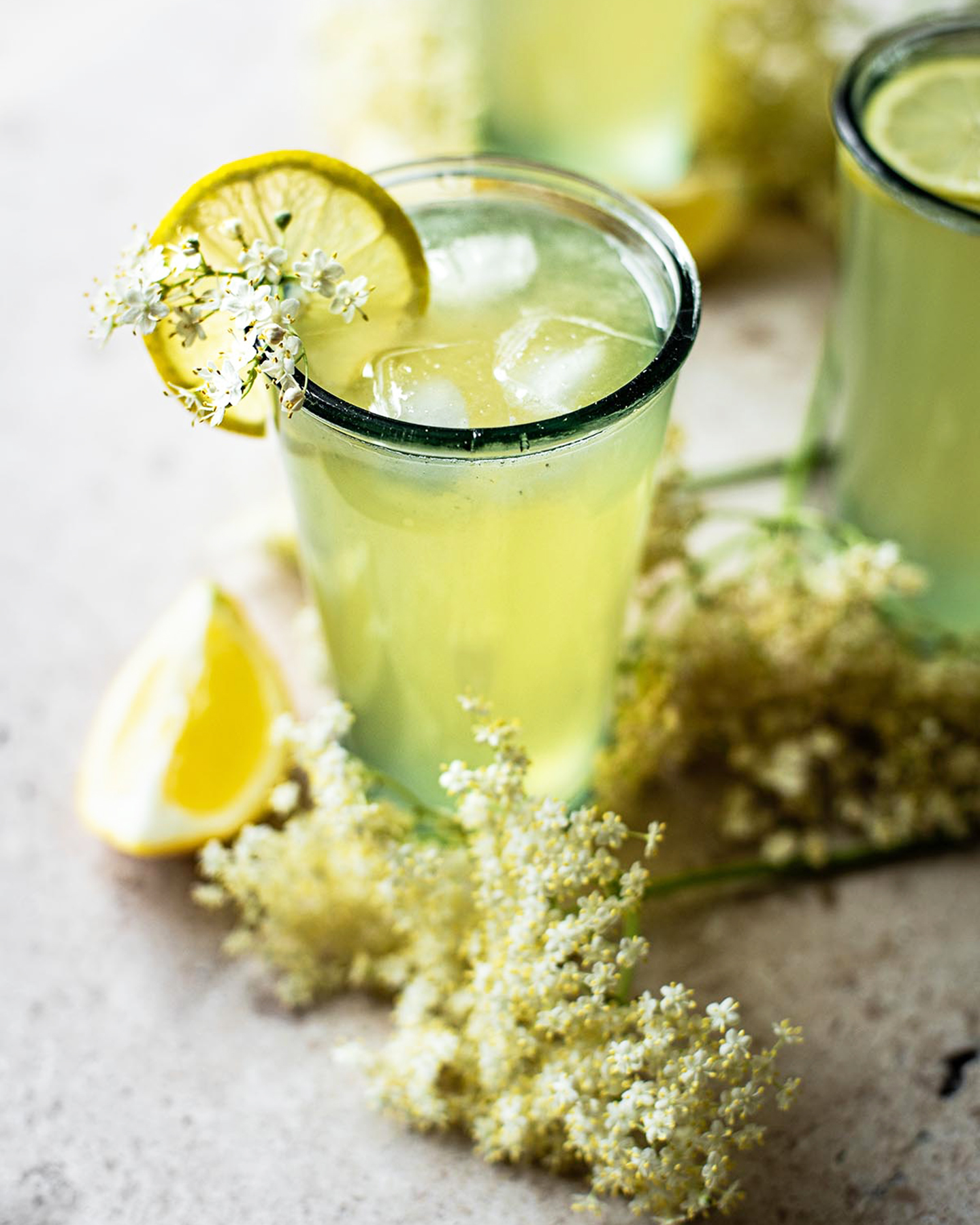 an elderflower lemonade in a glass with a lemon wedge and a sprig of elderflower on the table