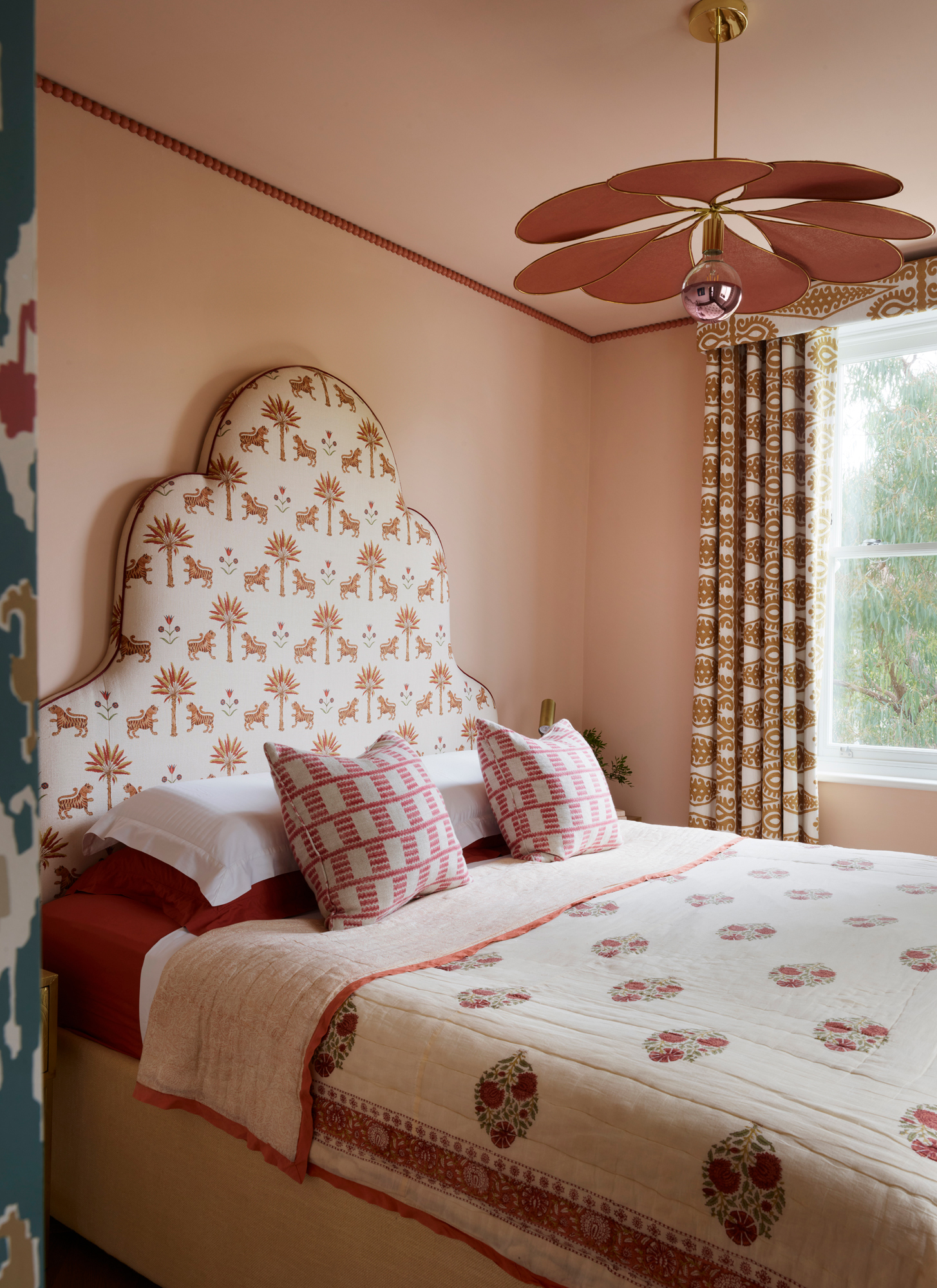 a bedroom with a large bed with a white patterned headboard, a pink flower shaped pendant light shade and a pink trim around the ceiling
