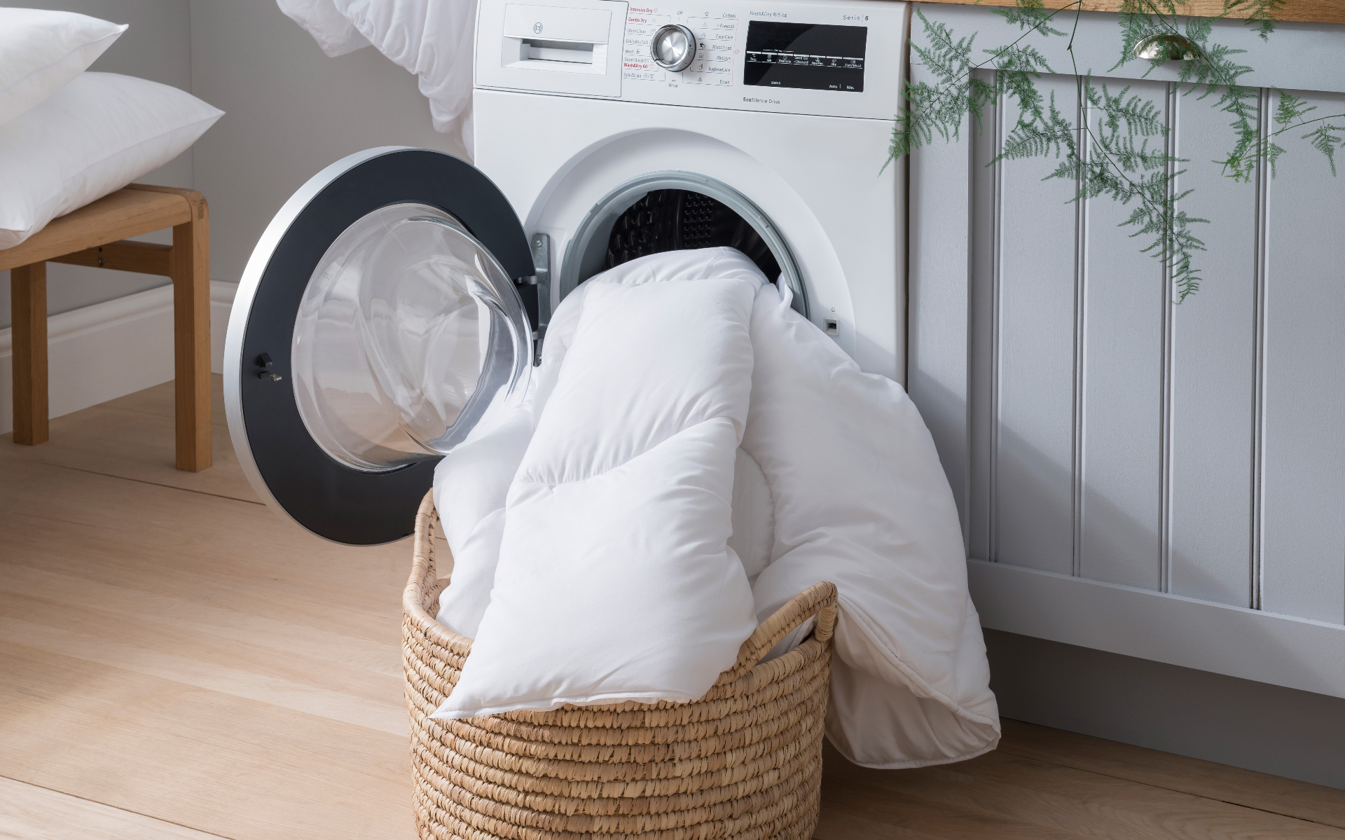 a duvet half in a washing machine and half in a woven laundry basket