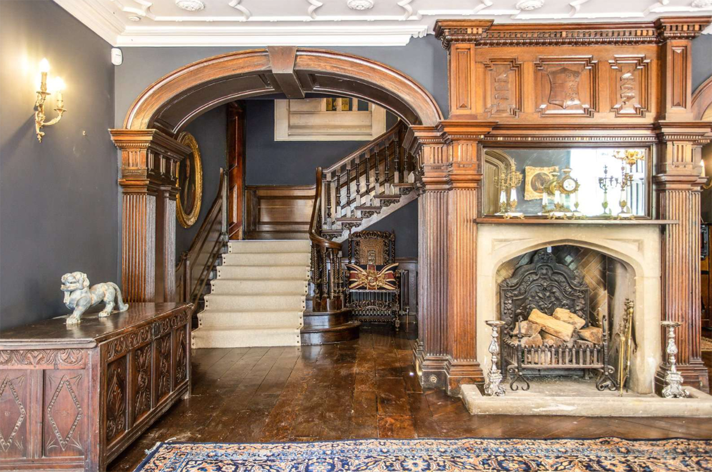 a grand hallway with a wooden sweeping staircase, a large wooden fireplace and a wooden arch