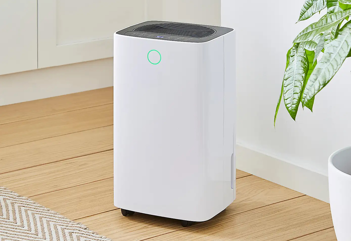 a white dehumidifier on a wooden floor next to a house plant