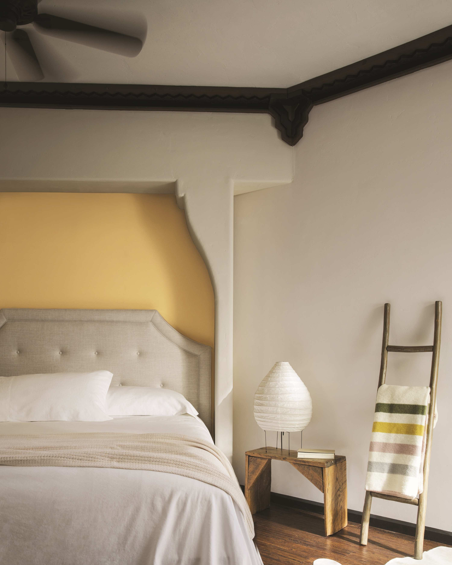 a bedroom with a large yellow headboard, a black border around the ceiling, a black ceiling fan and a large bed with white bedding