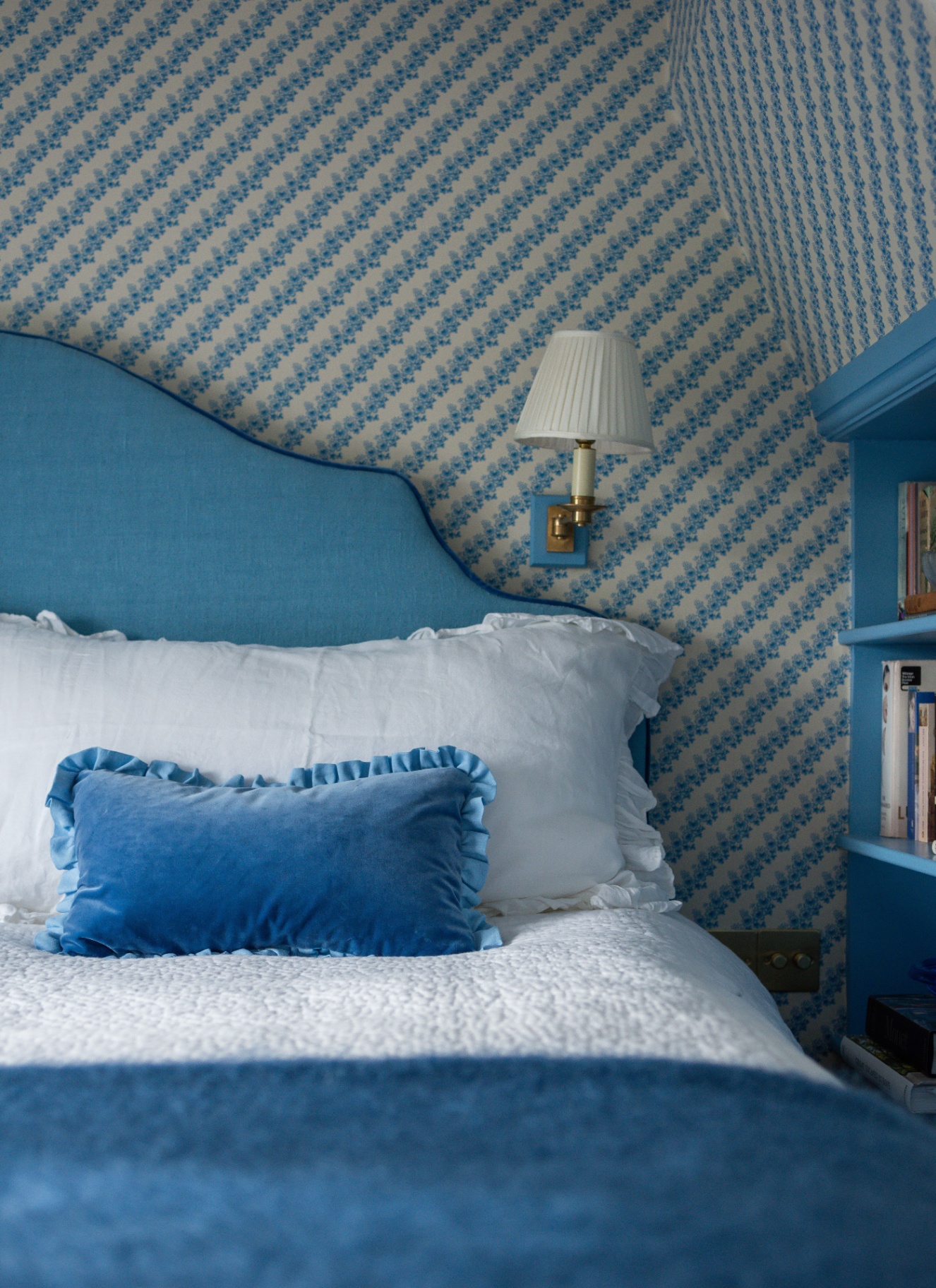 a close up of a bedroom with white and blue botanical wallpaper and a bed with a bright blue headboard