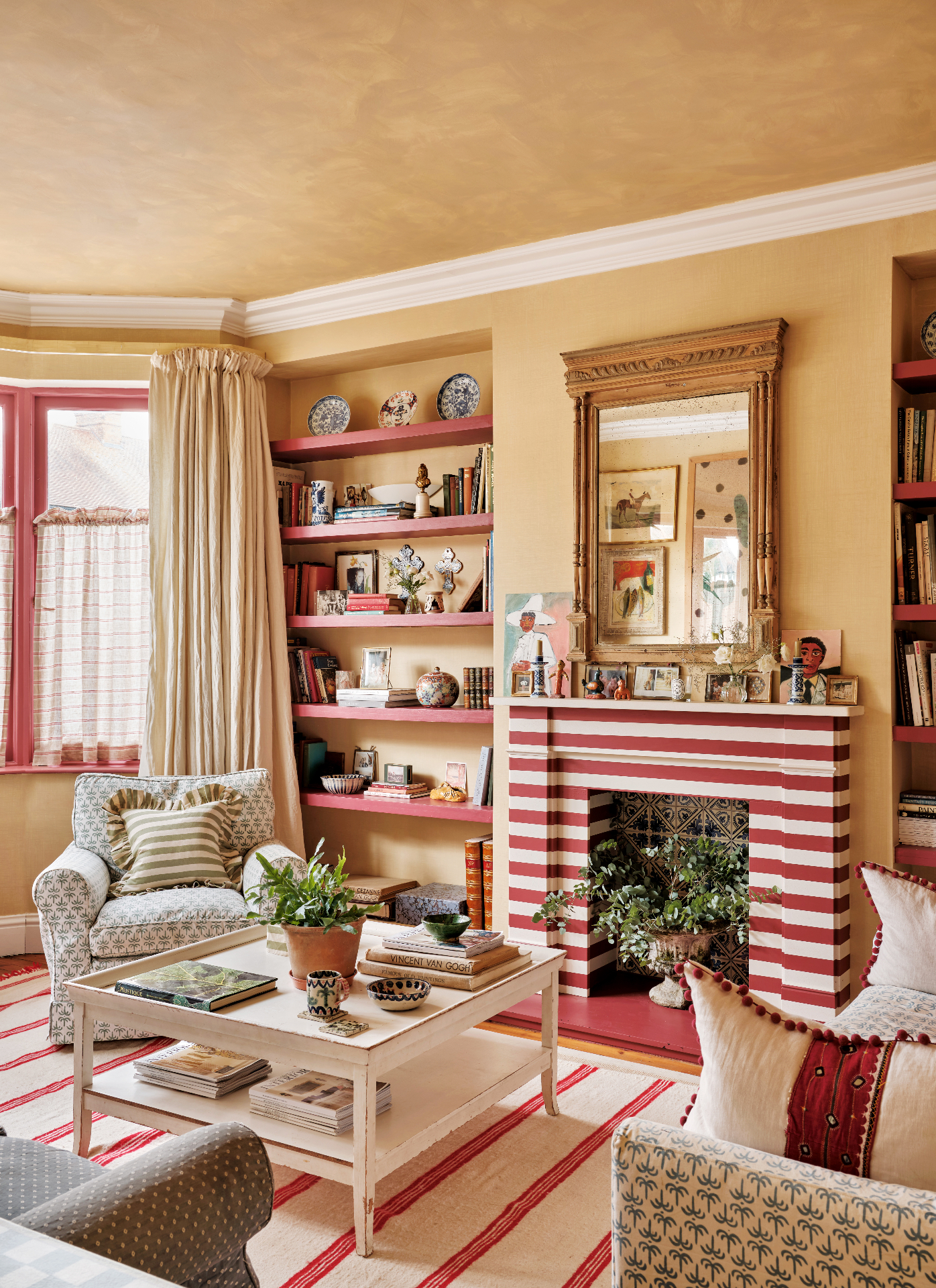 a living room with beige walls, a beige limewashed ceiling, a red and white striped fireplace with an ornate mirror above it and a white coffee table