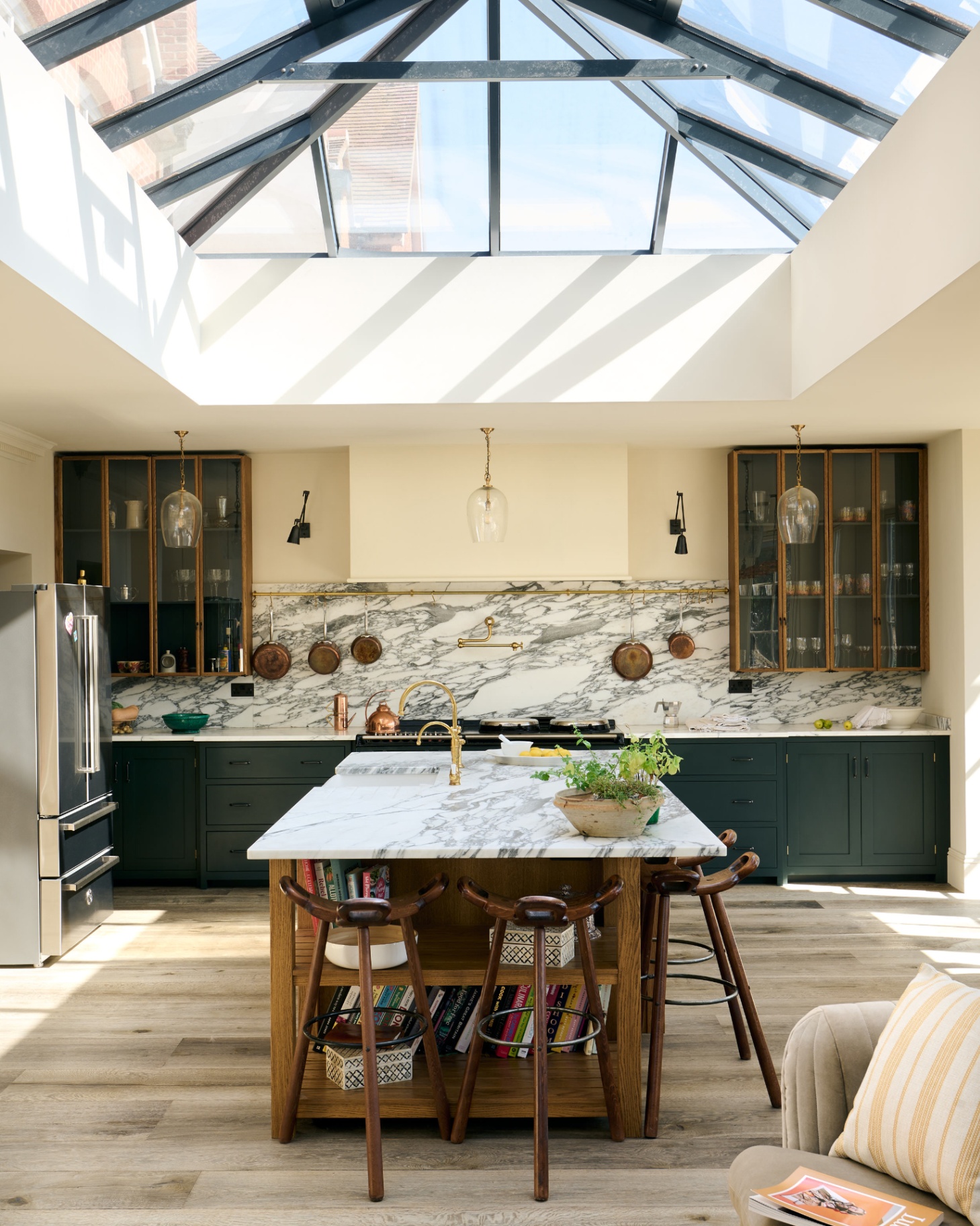 A KITCHEN with a large skylight, a wooden kitchen island with a white marble top, white marble splashbacks and 3 glass kitchen pendants