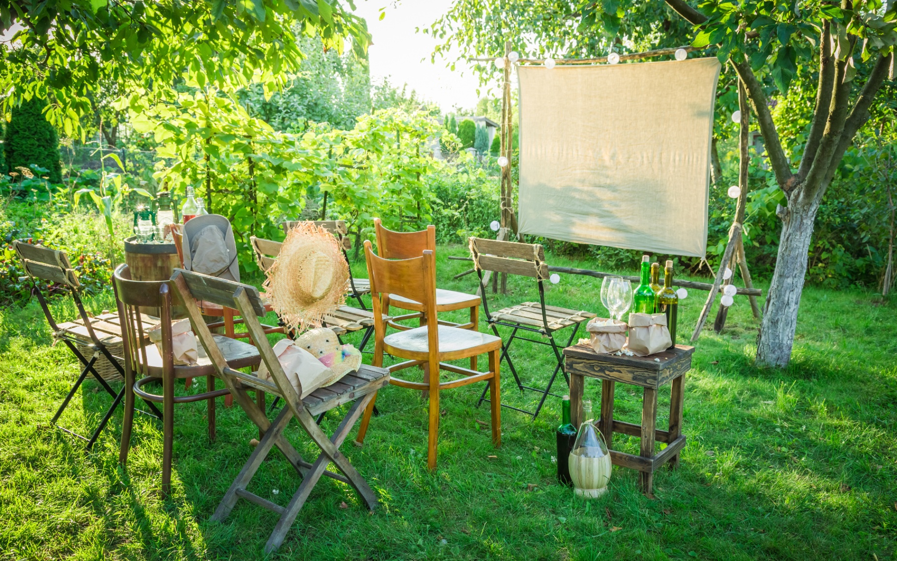 a garden with a cinema screen hung between two trees and rows of wooden garden chairs facing it to create an outdoor cinema