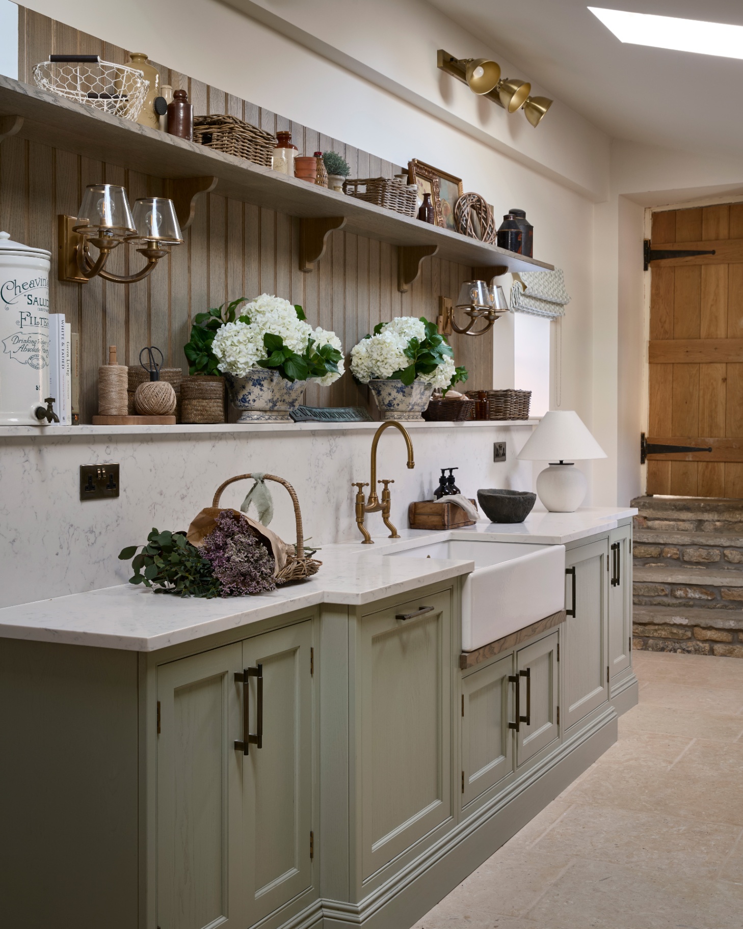 a utility room with sage green cabinets and open shelving filled with baskets, vases and decorative items