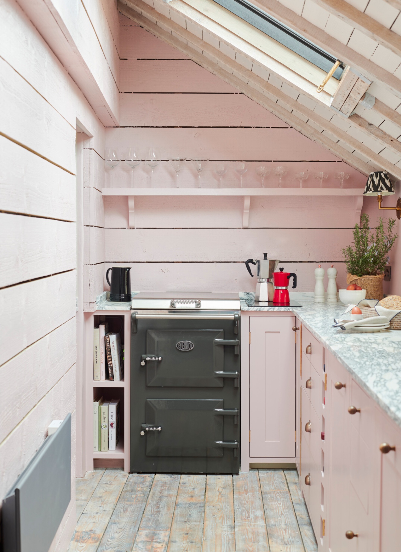 a narrow kitchen with sloped ceilings, pale pink cabinetry and walls and a slim dark grey everhot cooker