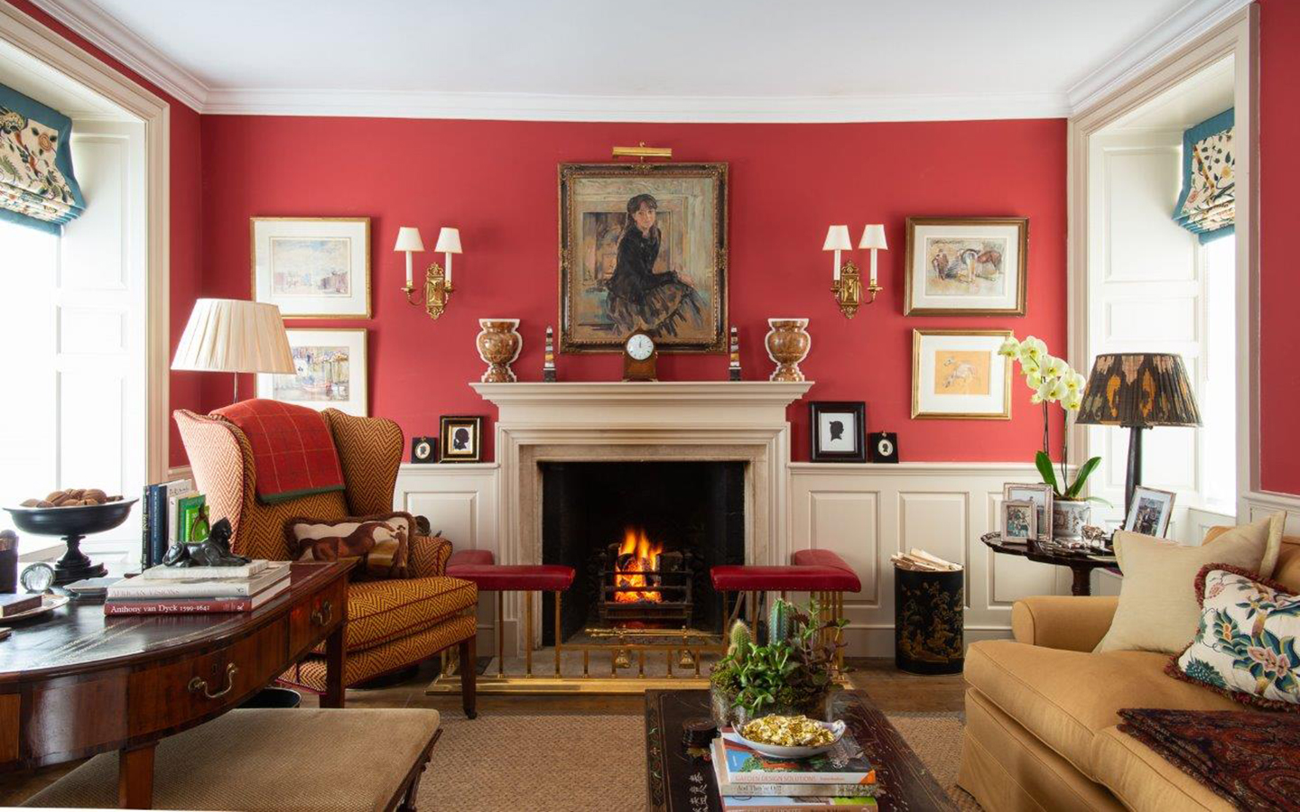 a grand red living room with a large open fireplace with a portrait painting above it, an orange patterned armchair next to it, a dark wooden table to the left and a yellow sofa to the left