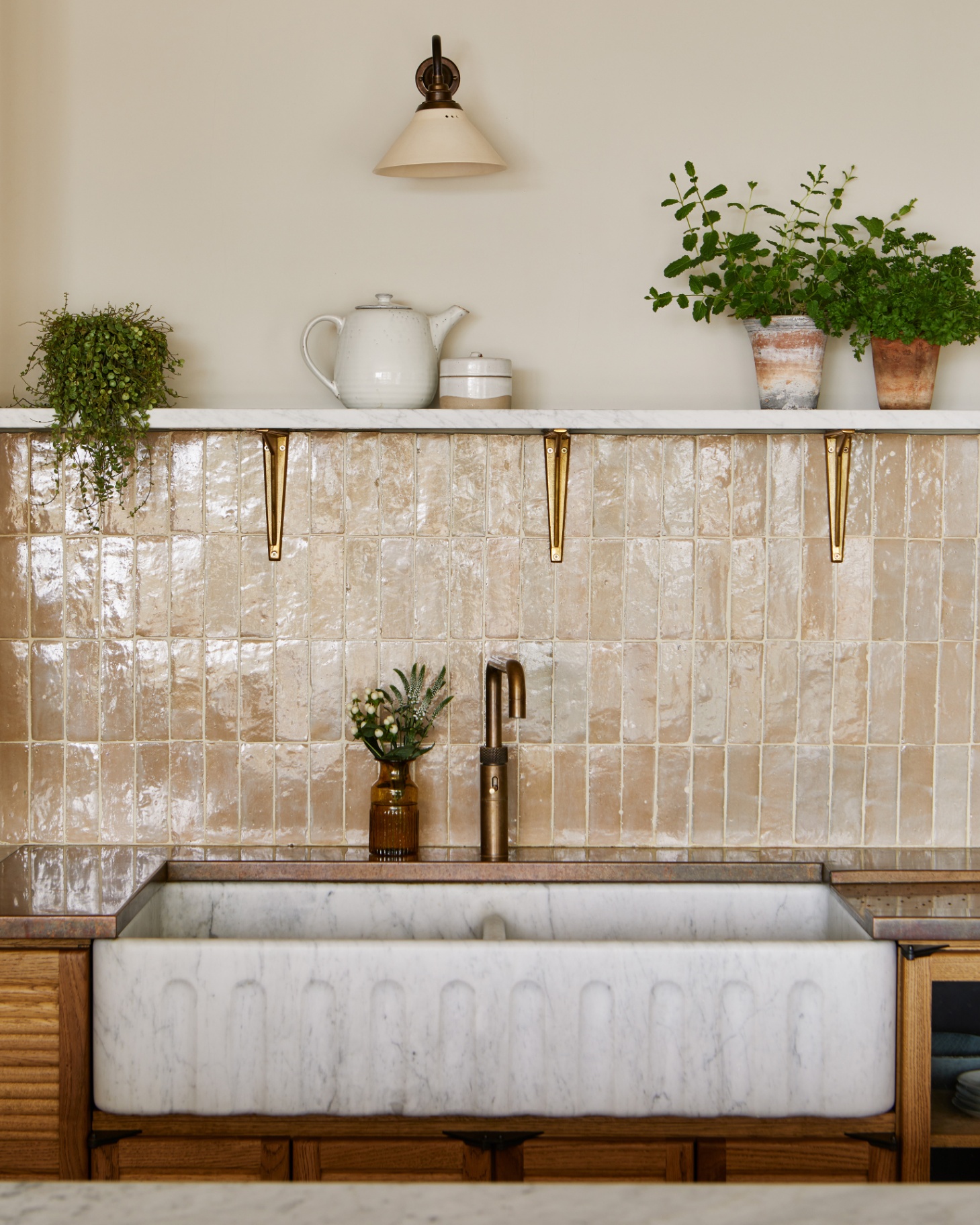 a kitchen sink area with neutral vertical tiles, a white belfast sink, wooden cabinets and an open shelf