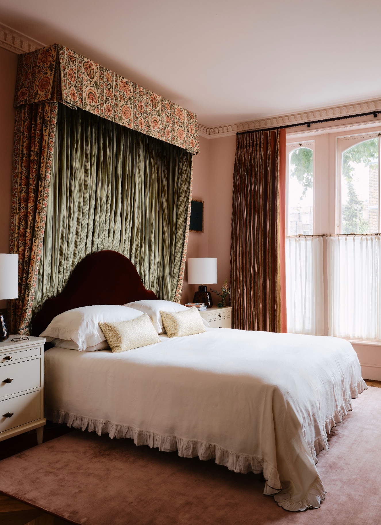 a bedroom with a floral canopy over a double bed with a dark red velvet headboard