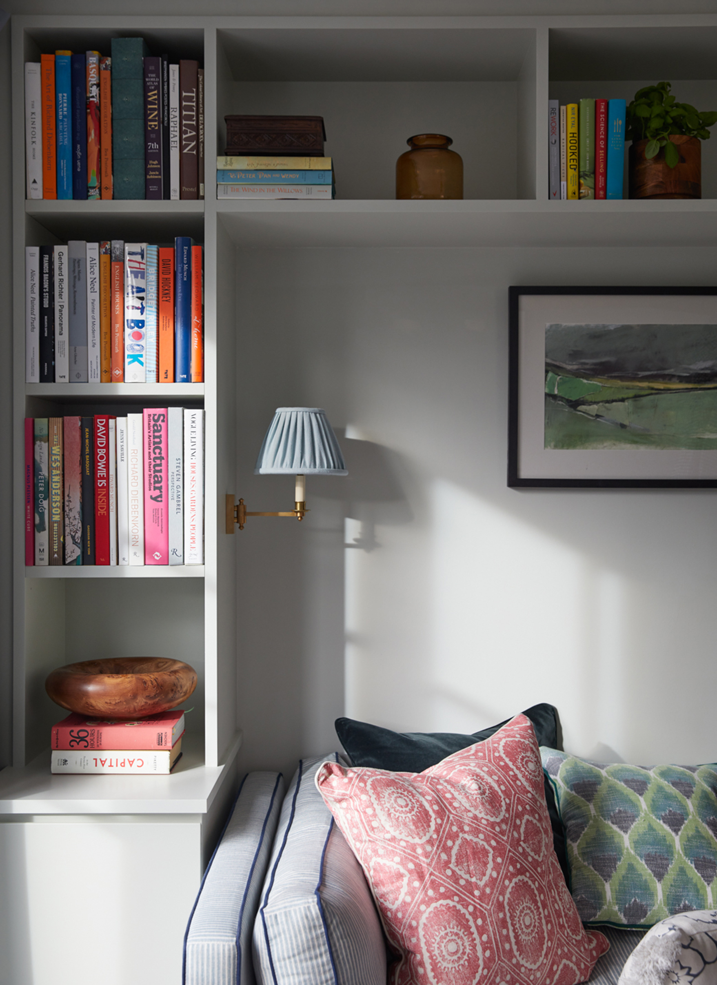 a close up of a living room with an l shaped bookshelf that goes alongside and above a blue and white striped sofa, filled with colourful books