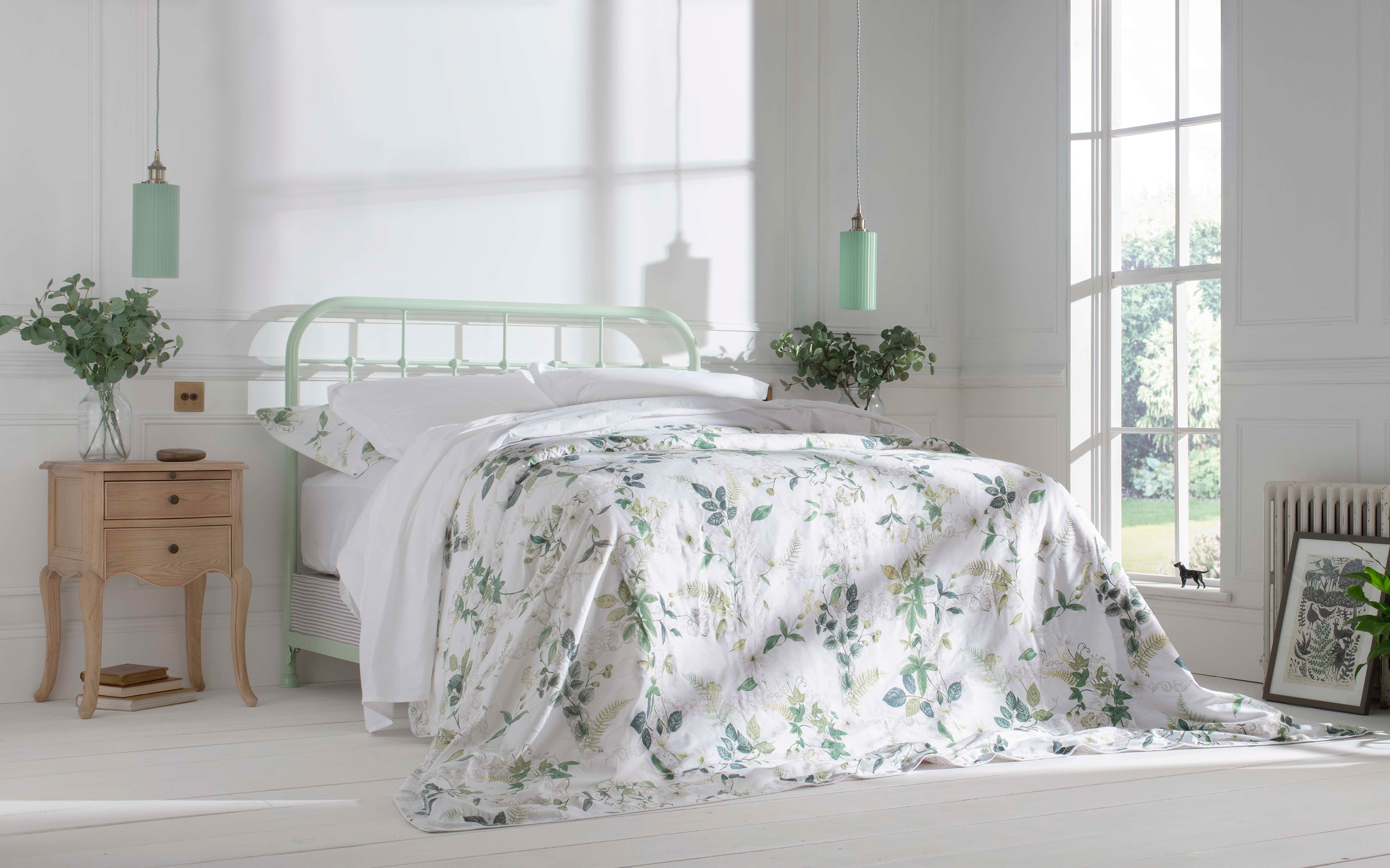 a sage green iron bed with white bedding and a floral bedspread