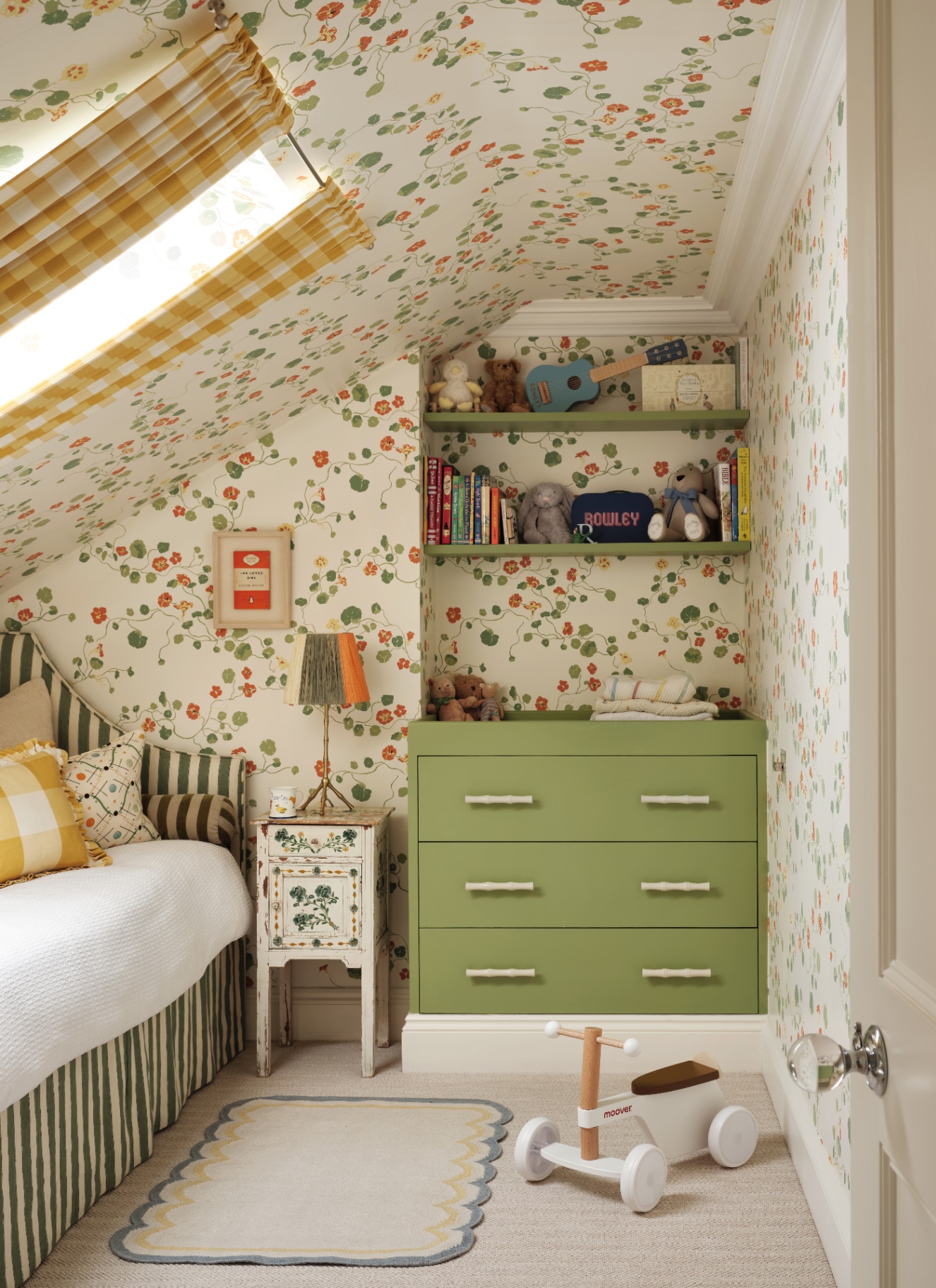 a children's bedroom with white and green botanical wallpaper, a green dresser and a bed with white bedding and a green and white striped valance