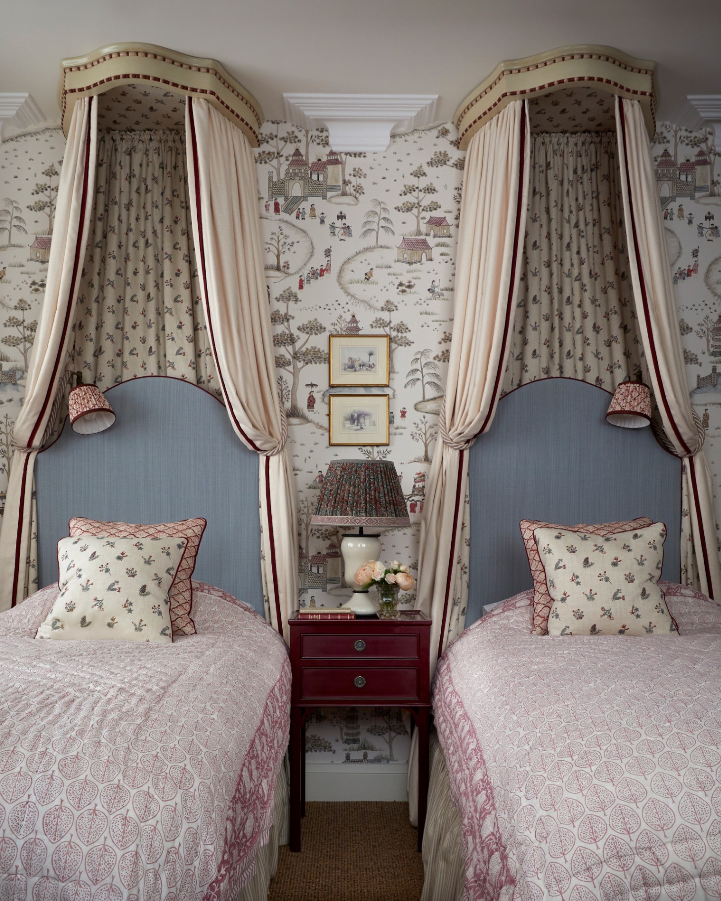 a traditional bedroom with twin beds with matching canopys, pink bedspread and blue headboards and a vintage wooden bedside table in the centre