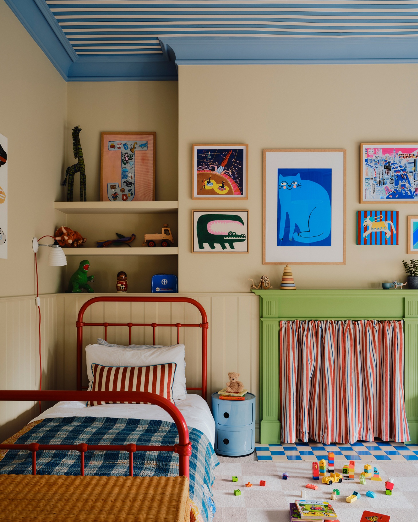 a children's bedroom with a blue and white striped ceiling, a green painted fireplace with a red and white stripe curtain covering the opening and a red iron frame bed