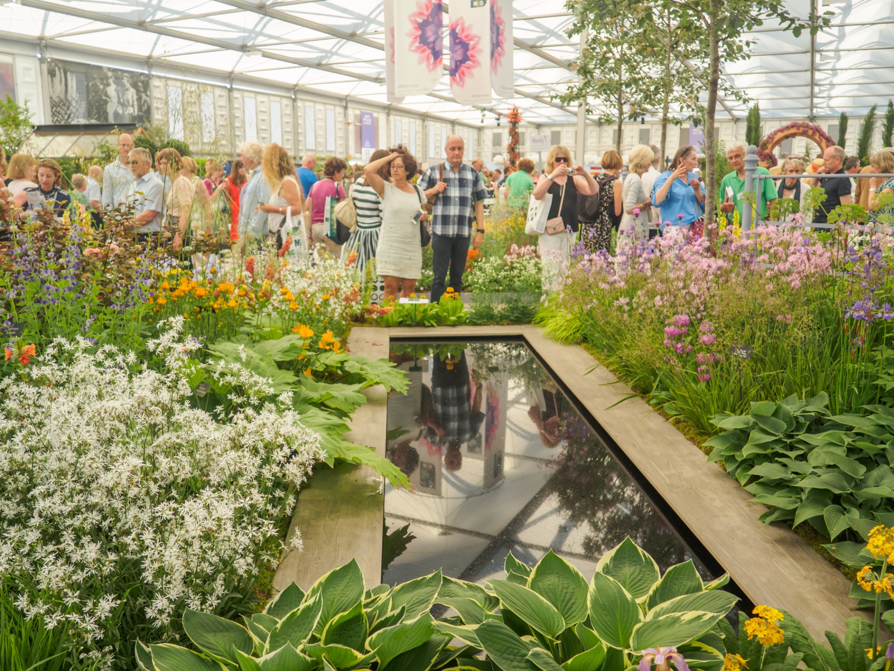 Inside a tent at the RHS Chelsea Flower Show, showing people in summer clothes admiring a garden inside a huge white tent