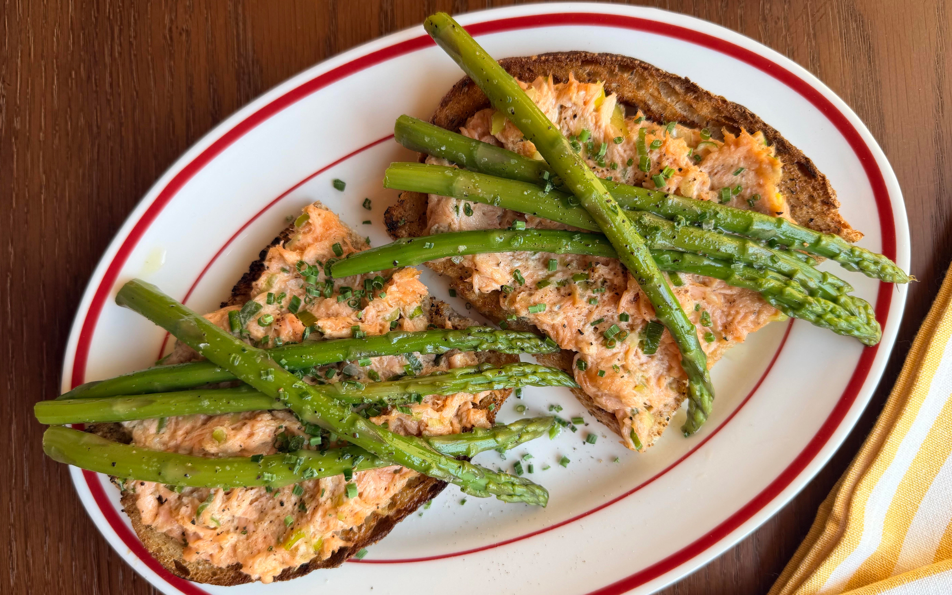 trout pate on toast with asparagus on a white and red plate on a wooden table