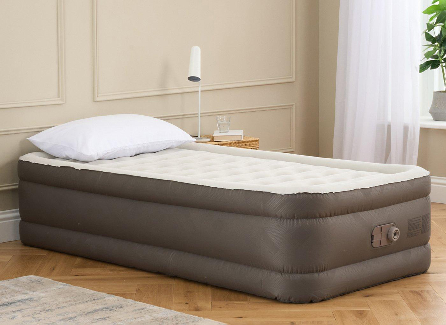 a dark grey and cream single air bed on a wooden floor against a beige panelled wall