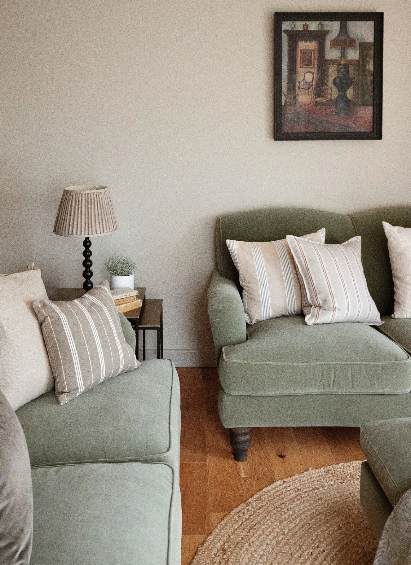 a sitting room with pale green velvet sofas, a black framed print on the wall, a round jute rug and a side table with a cream pleated lamp