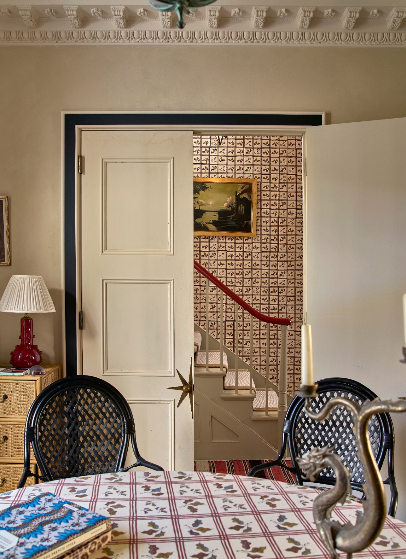 a dining room with a round table with two black rattan chairs and a large double open door looking out to the hallway