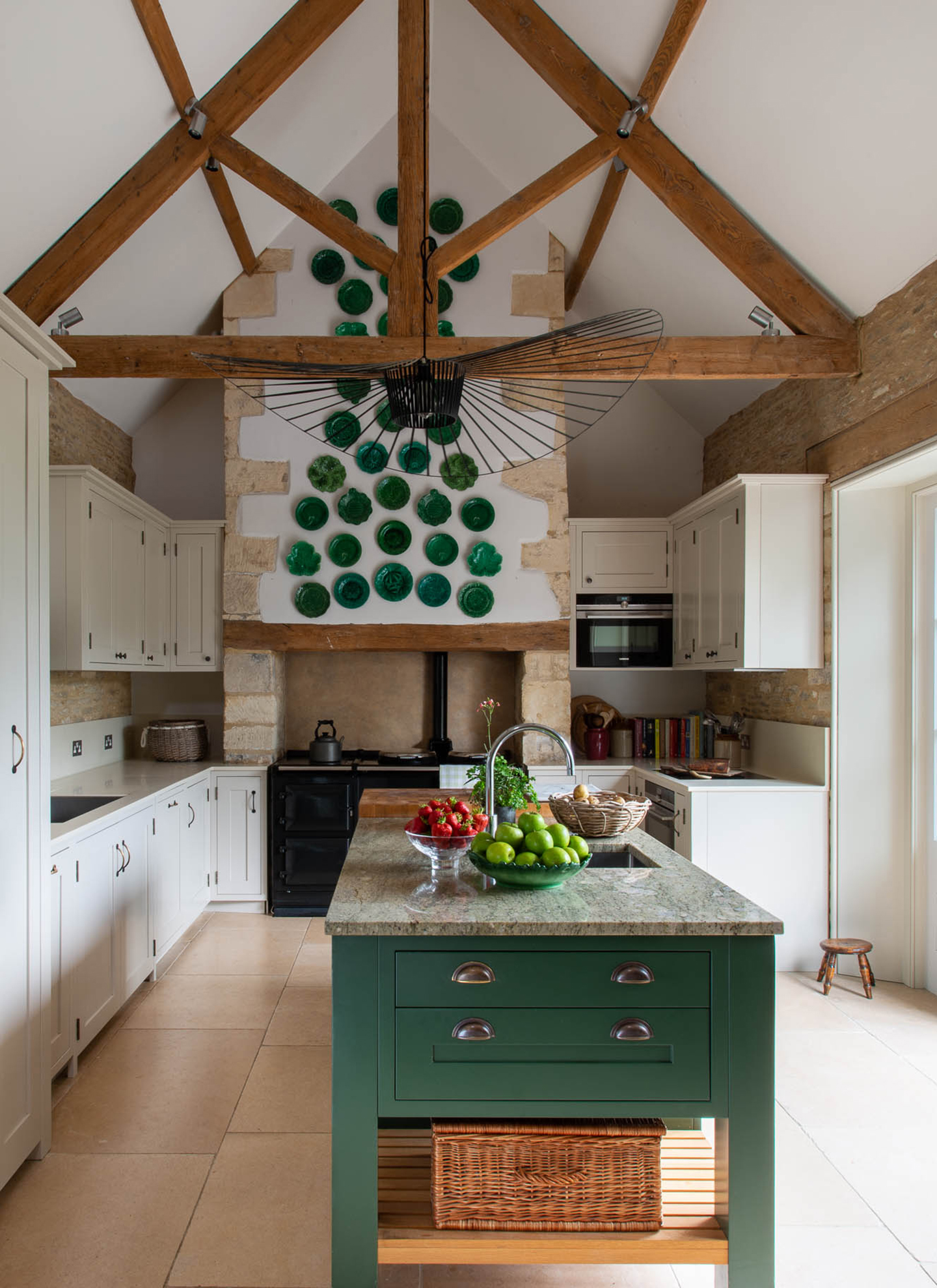 a country kitchen with high ceilings and wooden beams, a selection of green plates hanging on the wall and a large green marble topped kitchen island