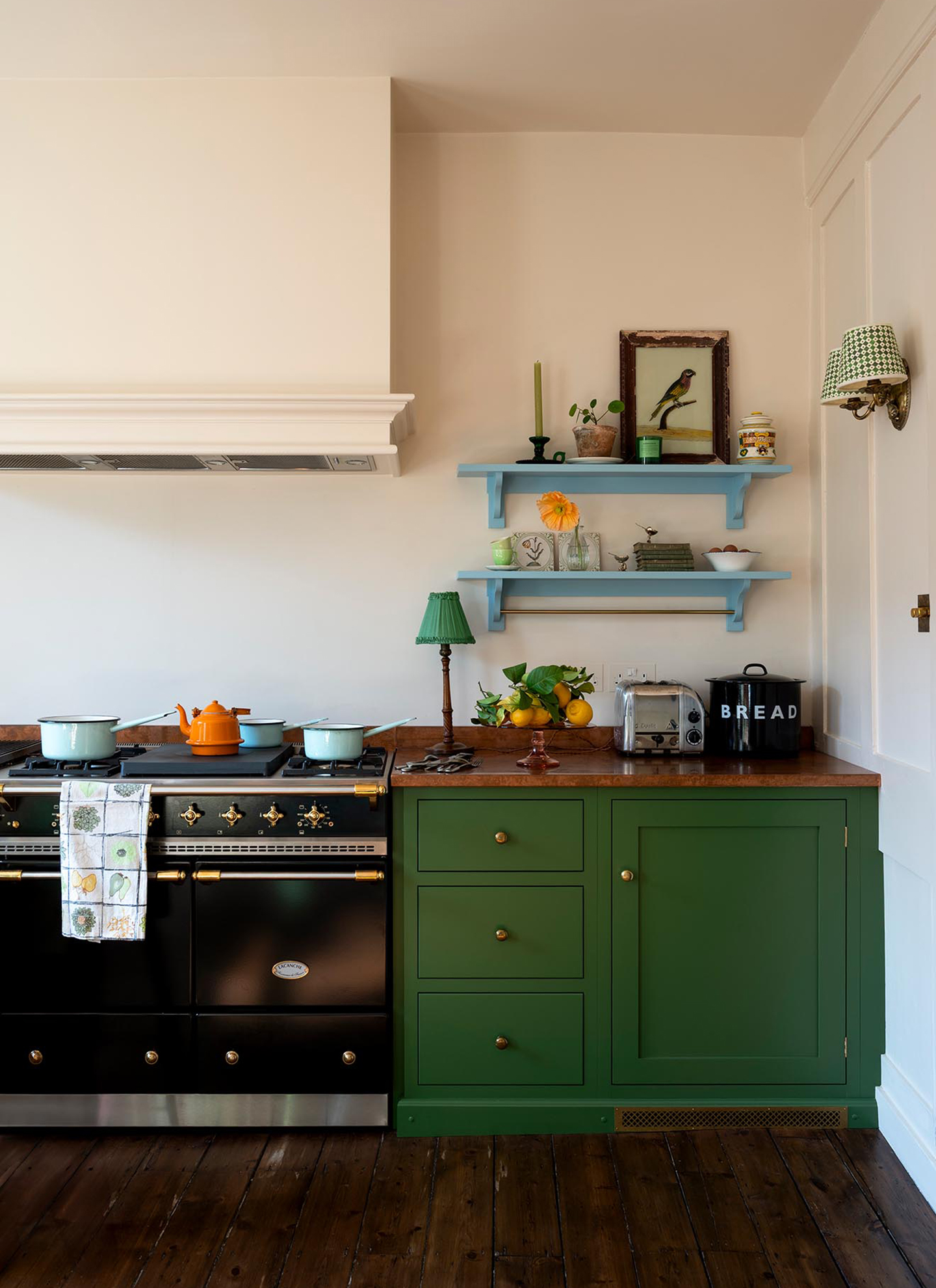 a kitchen with green cabinets, dark wooden flooring and two blue open shelves