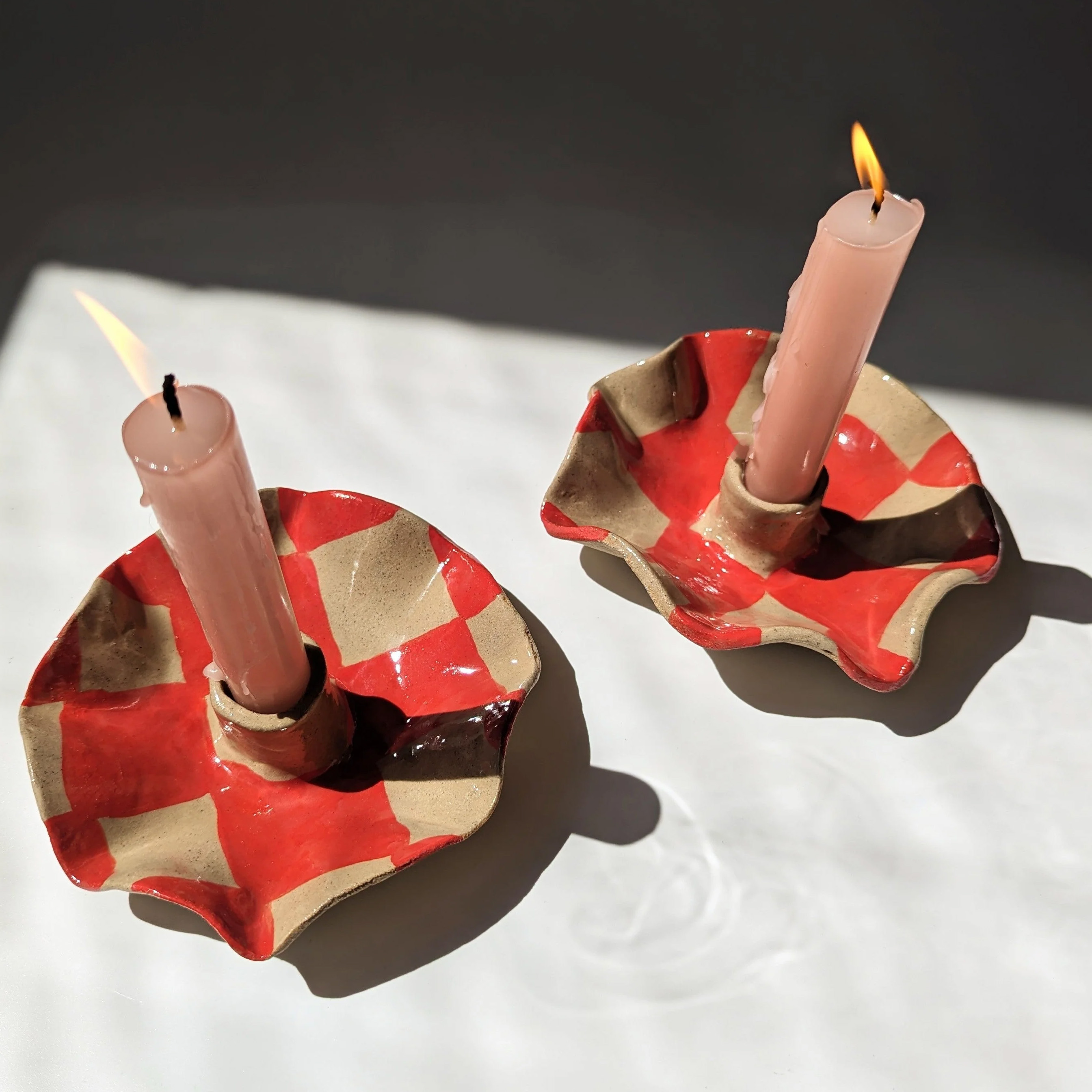 two round red checkerboard candle stick holders, each with a burning candle stick
