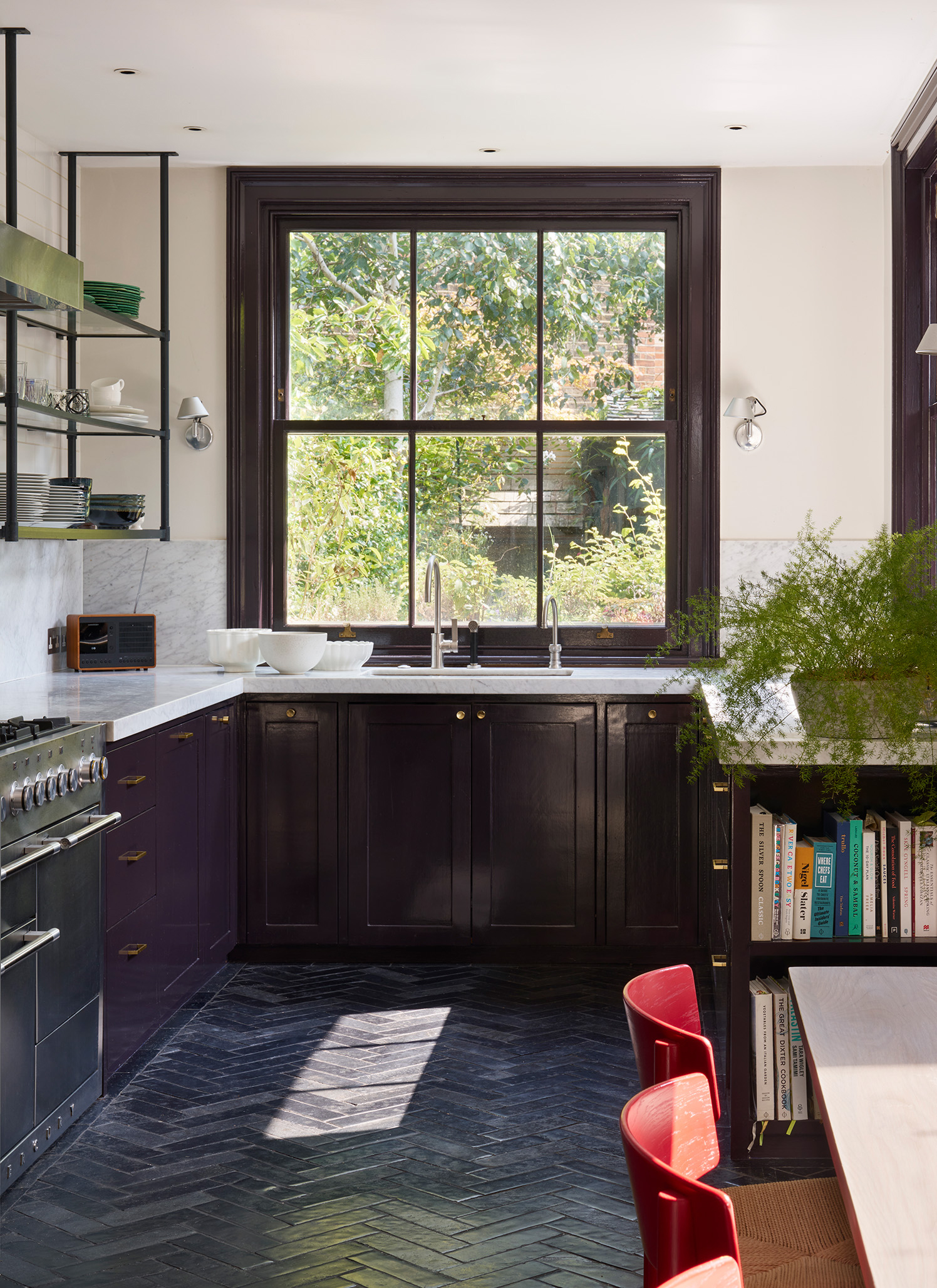 a small kitchen with black cabinetry, a large sash window, black stone flooring, marble countertops and books slotted into the side of a cabinet