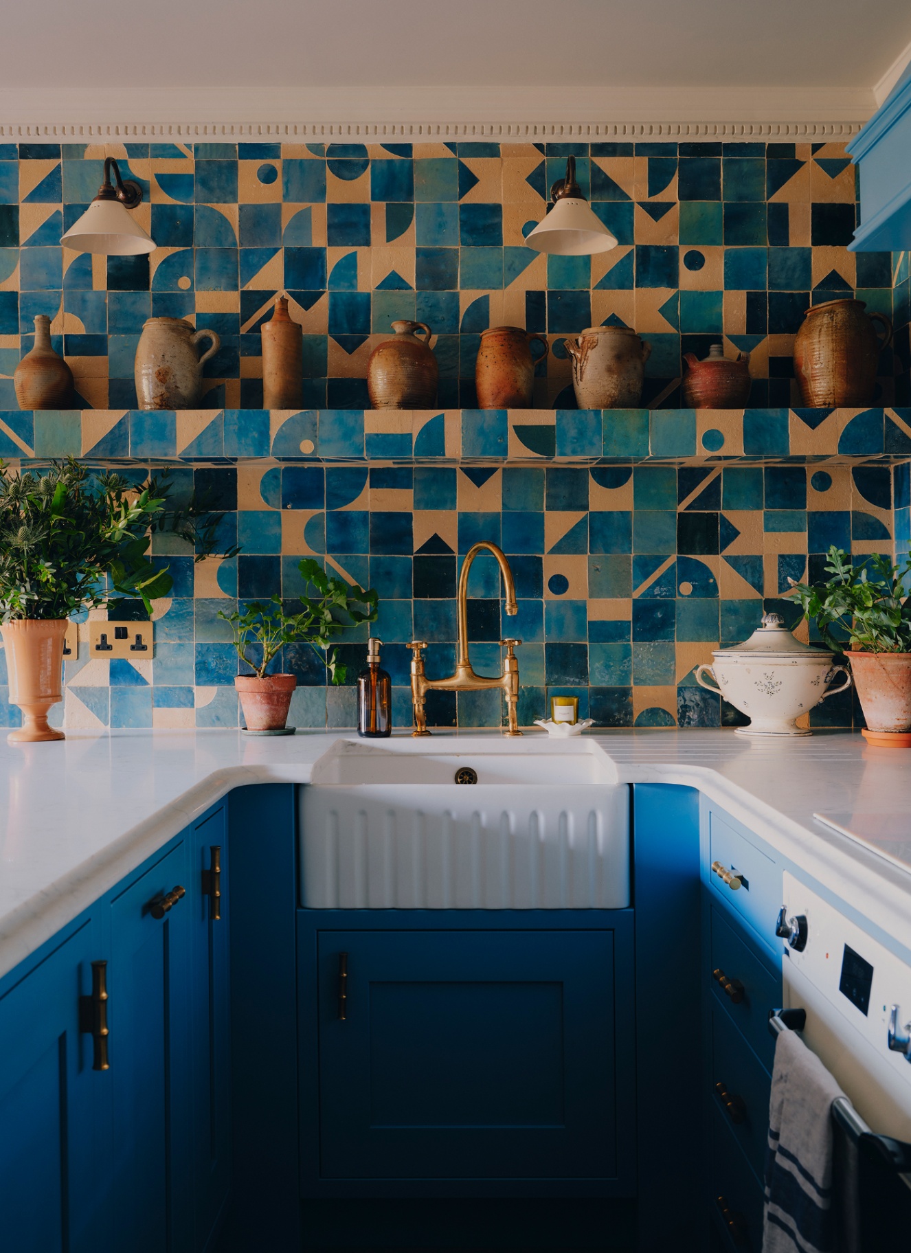 a small kitchen with bold geometric tiles on the walls in blue and terracotta and royal blue cabinetry