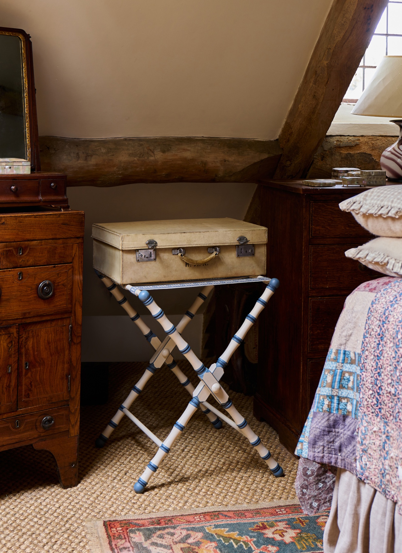 close up of a bedroom corner with wooden beams, antique wooden furniture and a folding luggage holder with a vintage suitcase