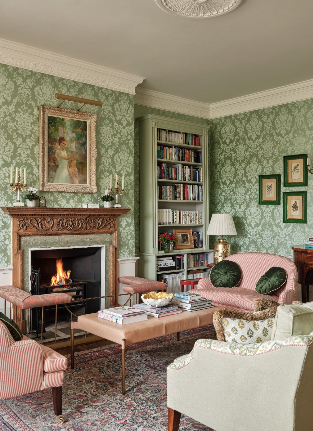 a living room with a large shaded chandelier, two green sofas with floral cushions, two green and white floral armchairs, a clear glass coffee table with a red tray and salmon pink walls