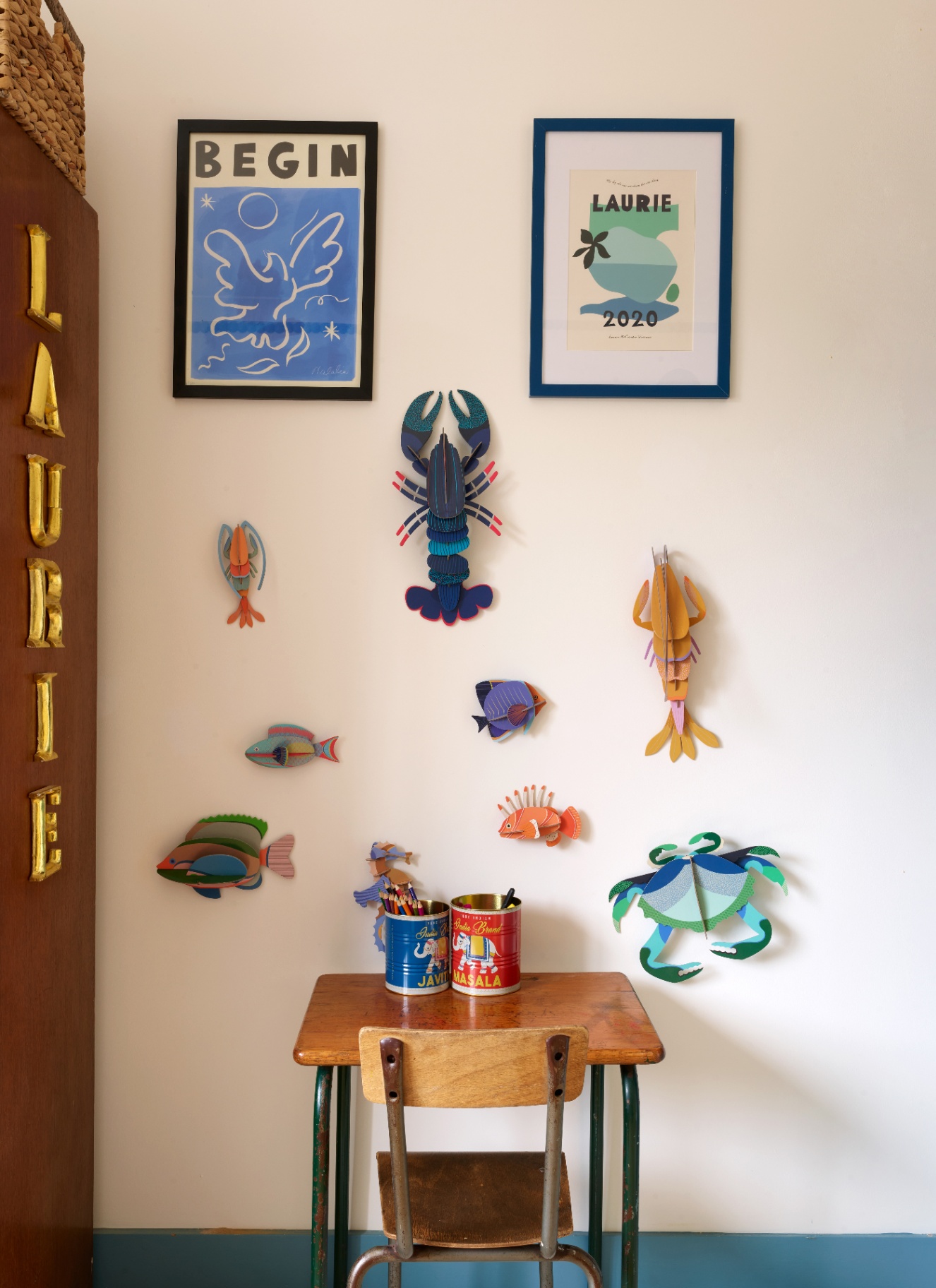 a close up of a corner in a childrens room with white walls, a small wooden desk and chair with paper marine animals on the wall
