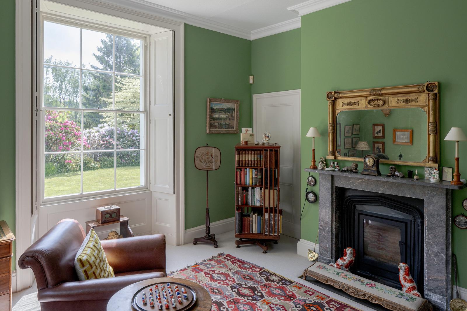 a living room with a large window, green walls and a grey marble fireplace