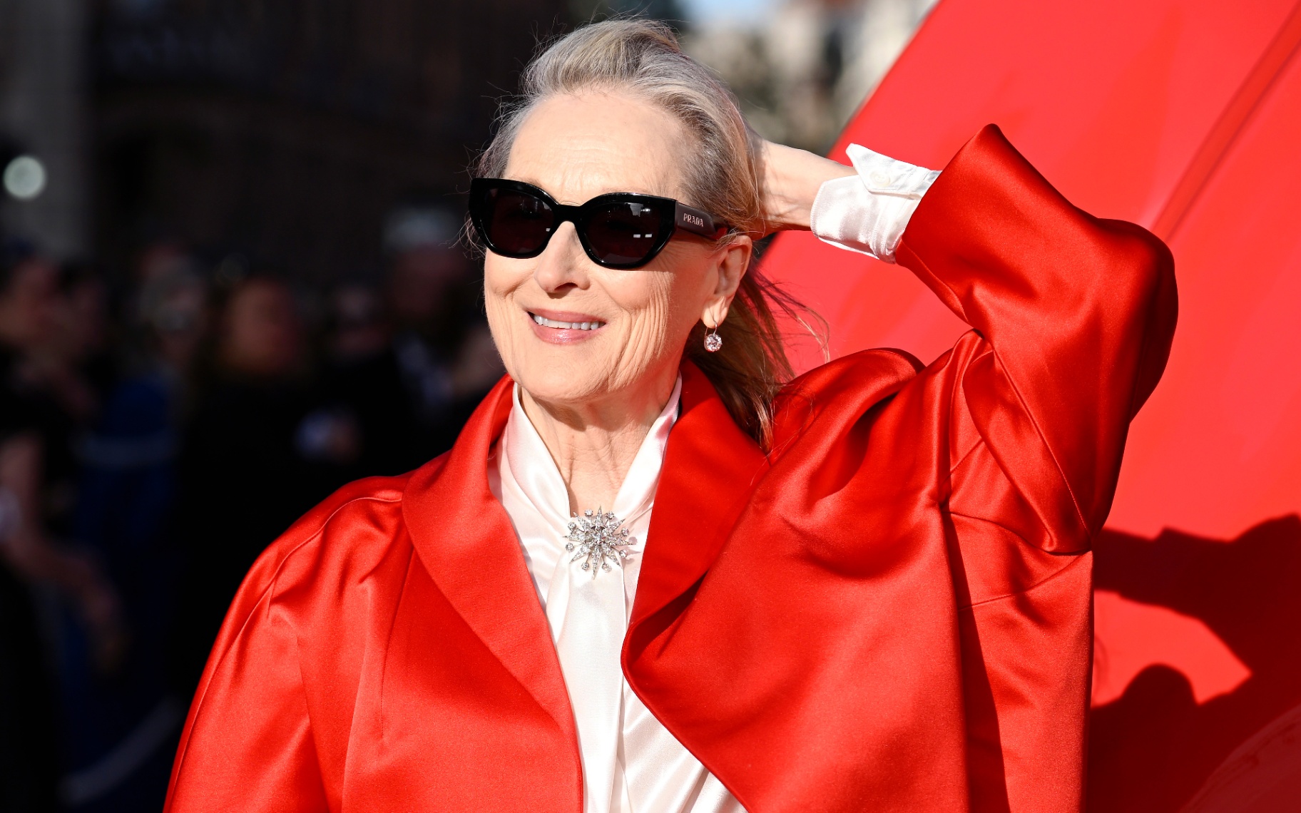 Meryl Streep wearing black sunglasses and a red coat at the devil wears prada 2 premiere in London